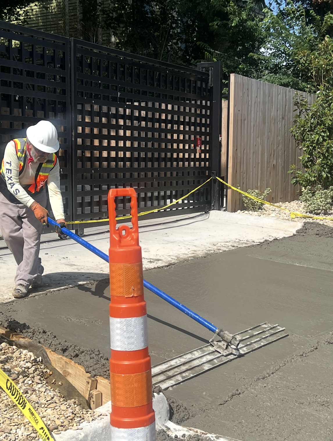 Worker using a long-handled finishing tool on freshly placed sidewalk concrete.