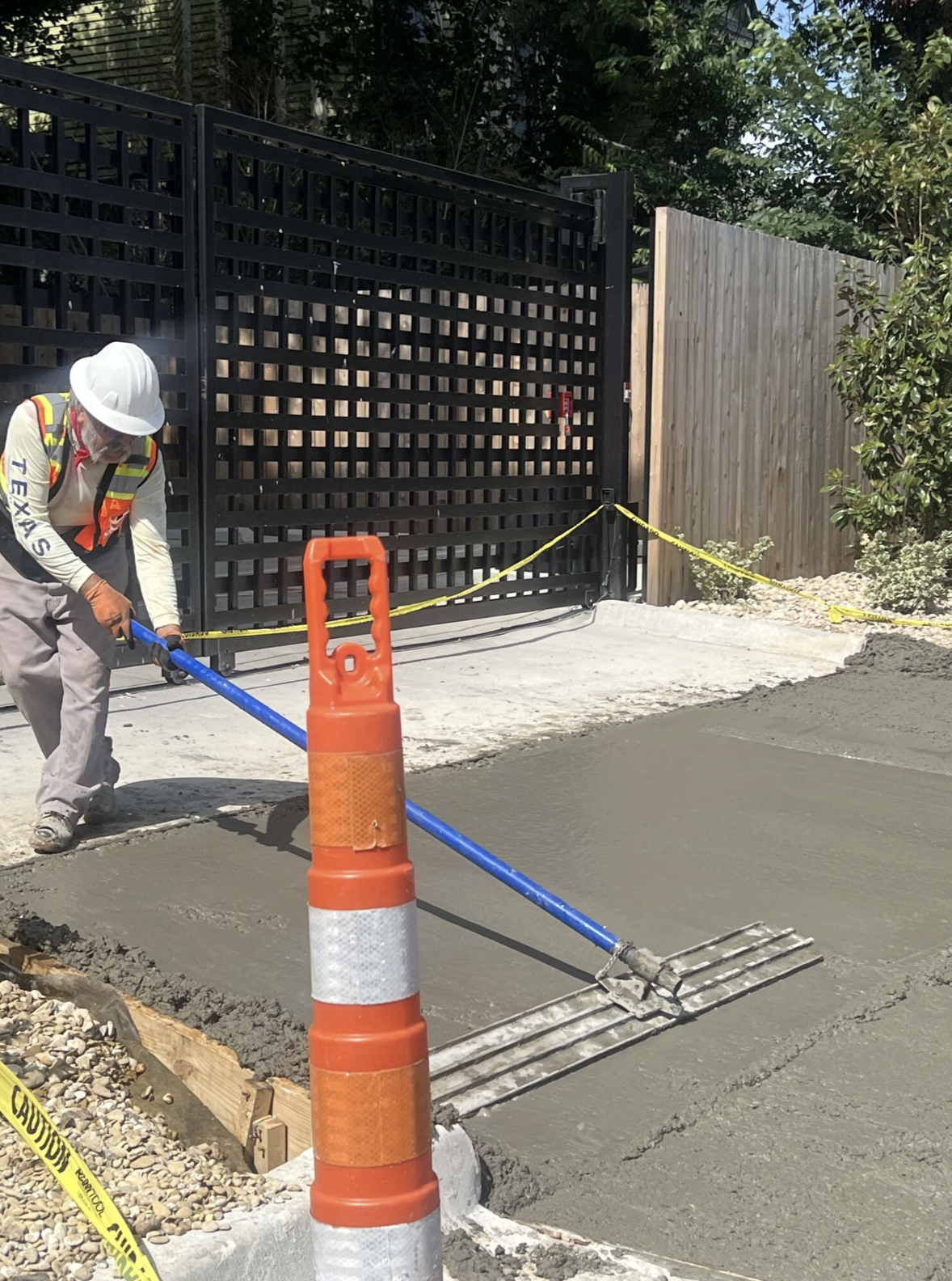 8 Pillars Concrete worker finishing replacement sidewalk concrete beside a black gate