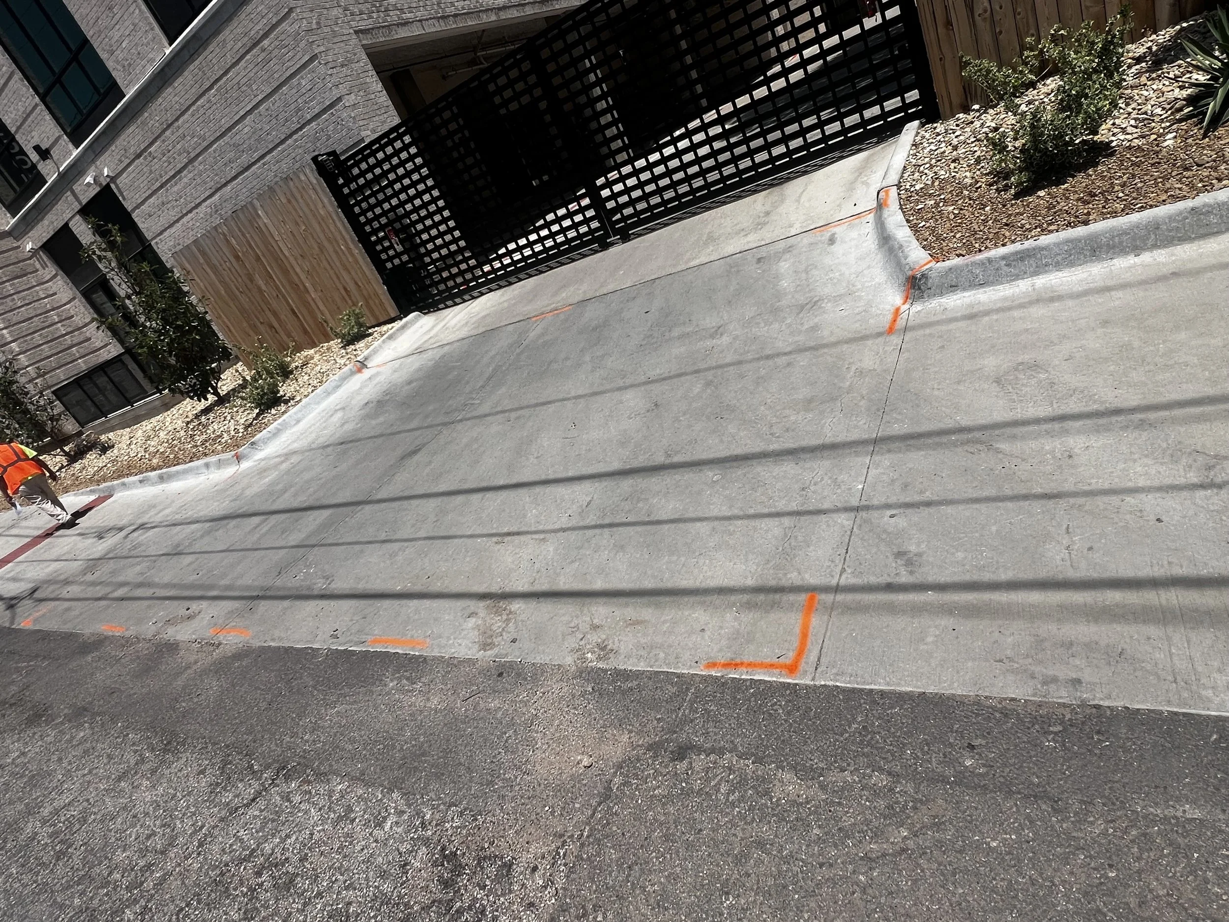 Completed concrete sidewalk with joints beside a black gate and landscaped entrance.