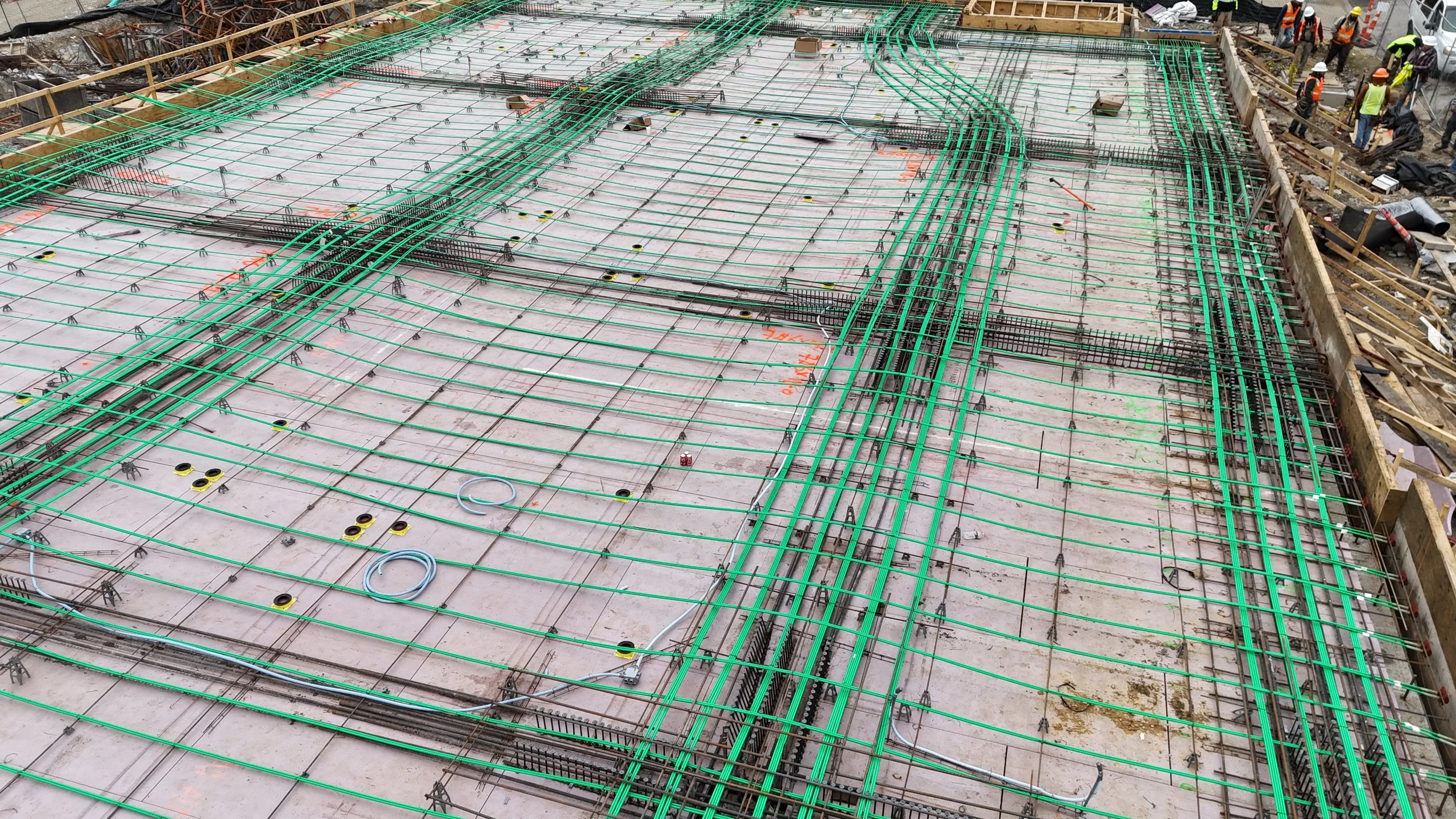 Close view of a steel reinforcement grid and bundled green tubing arranged across a deck before concrete placement.