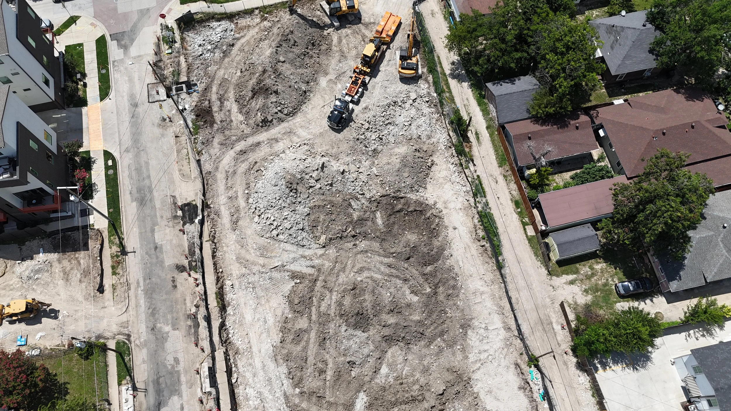Top-down aerial view of an excavated site with earthmoving equipment between neighboring properties.
