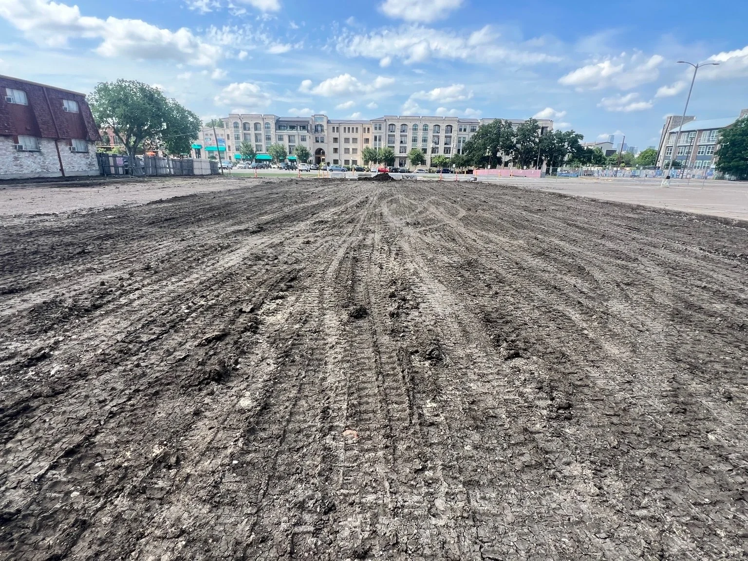 Wide view of a rough graded parking lot with buildings in the background.