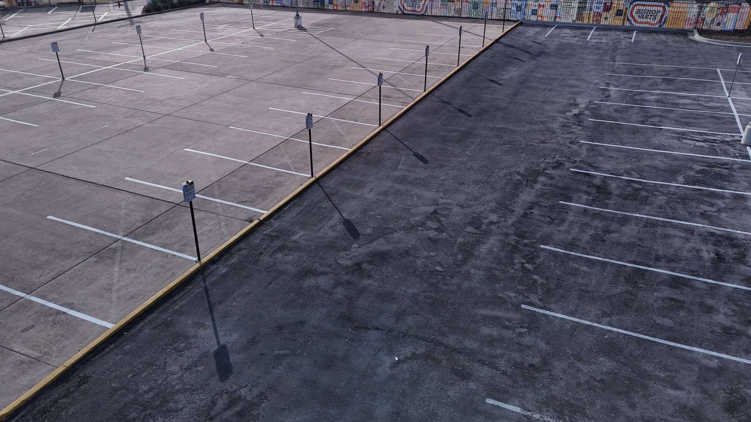 Aerial view of a striped parking lot with a yellow curb separating two paved areas.