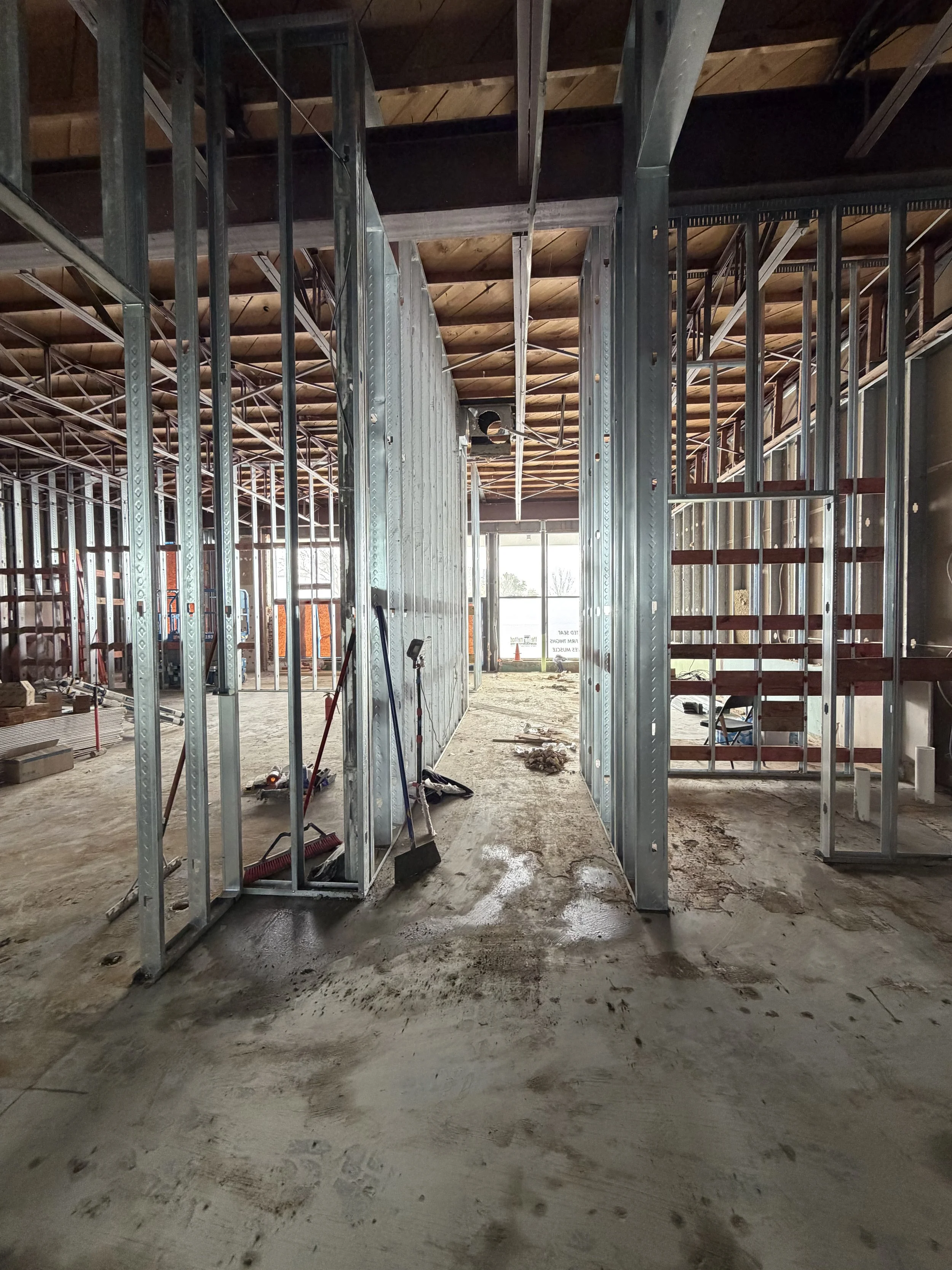 View through unfinished metal stud partitions toward a window, with construction materials on the floor.
