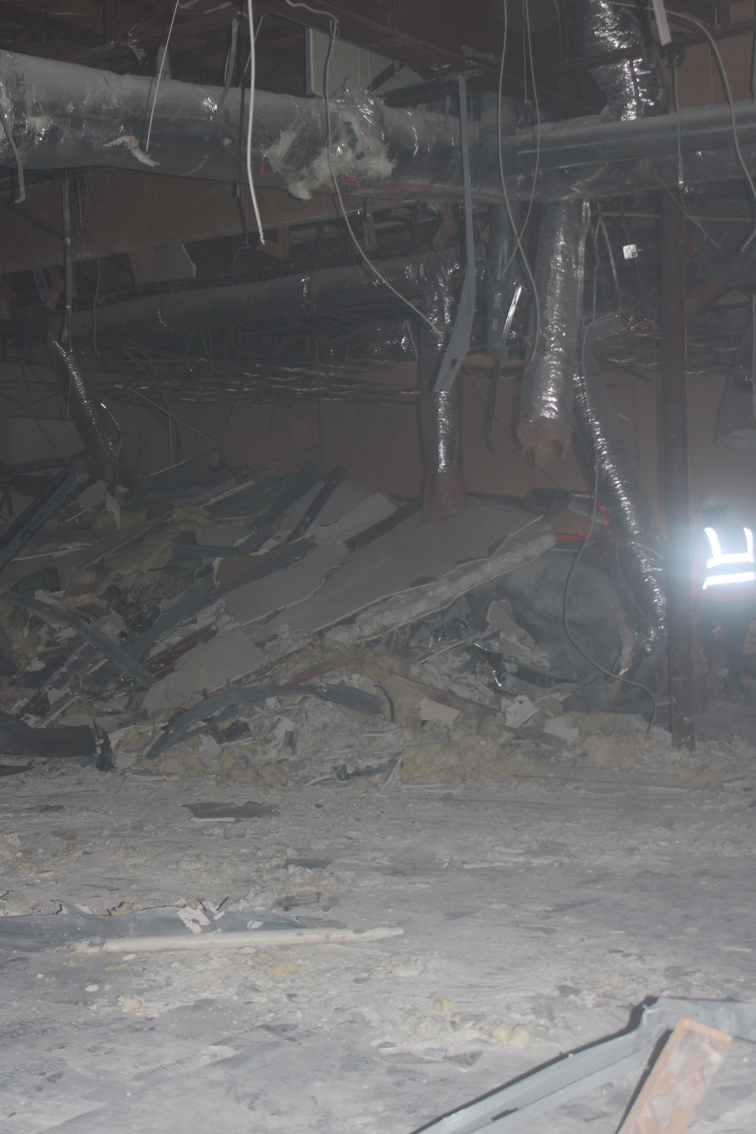 Demolition debris on an interior floor beneath exposed overhead ducts and pipes.