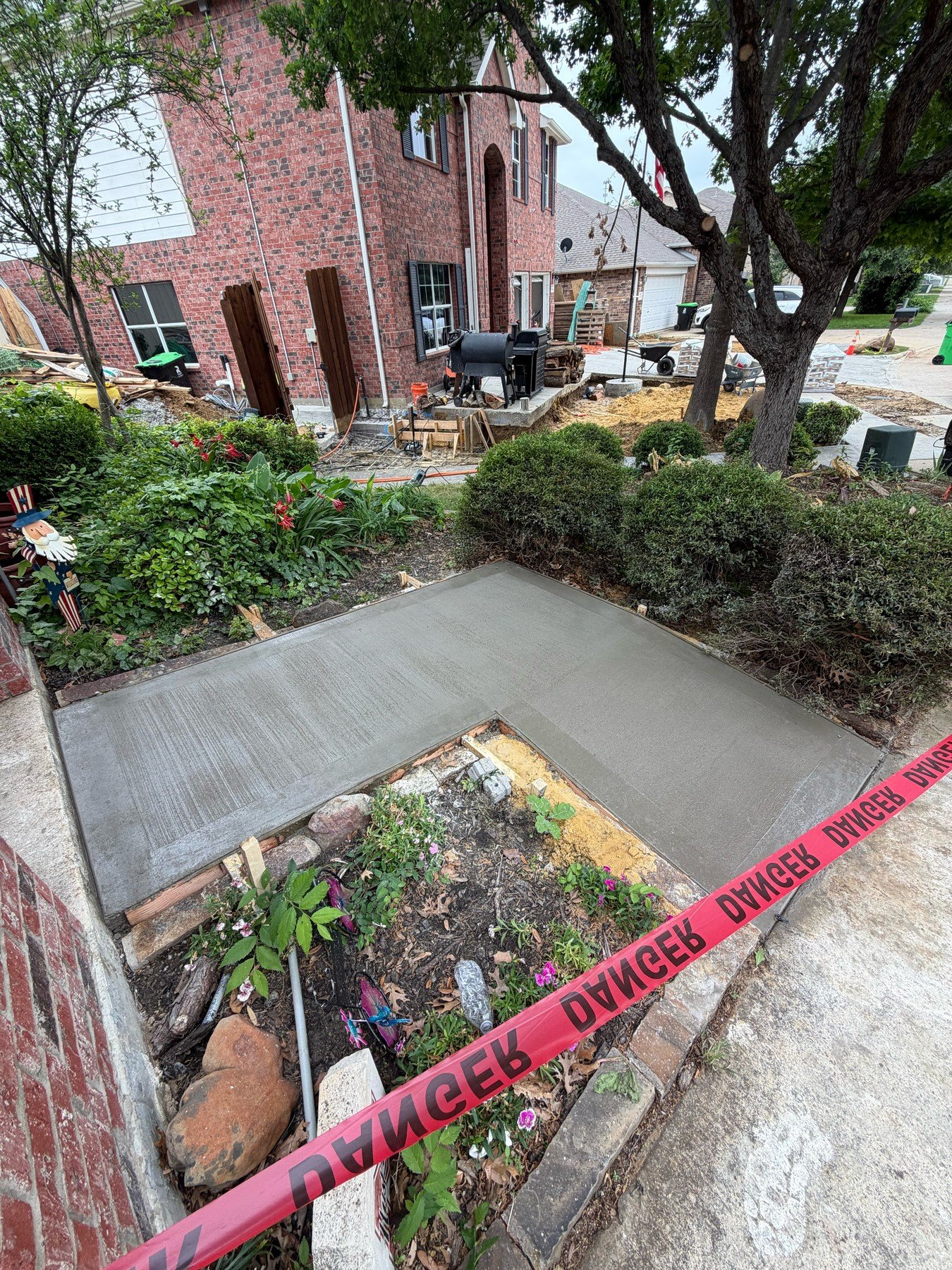 Fresh concrete walkway wraps around planted beds at a residential entrance.