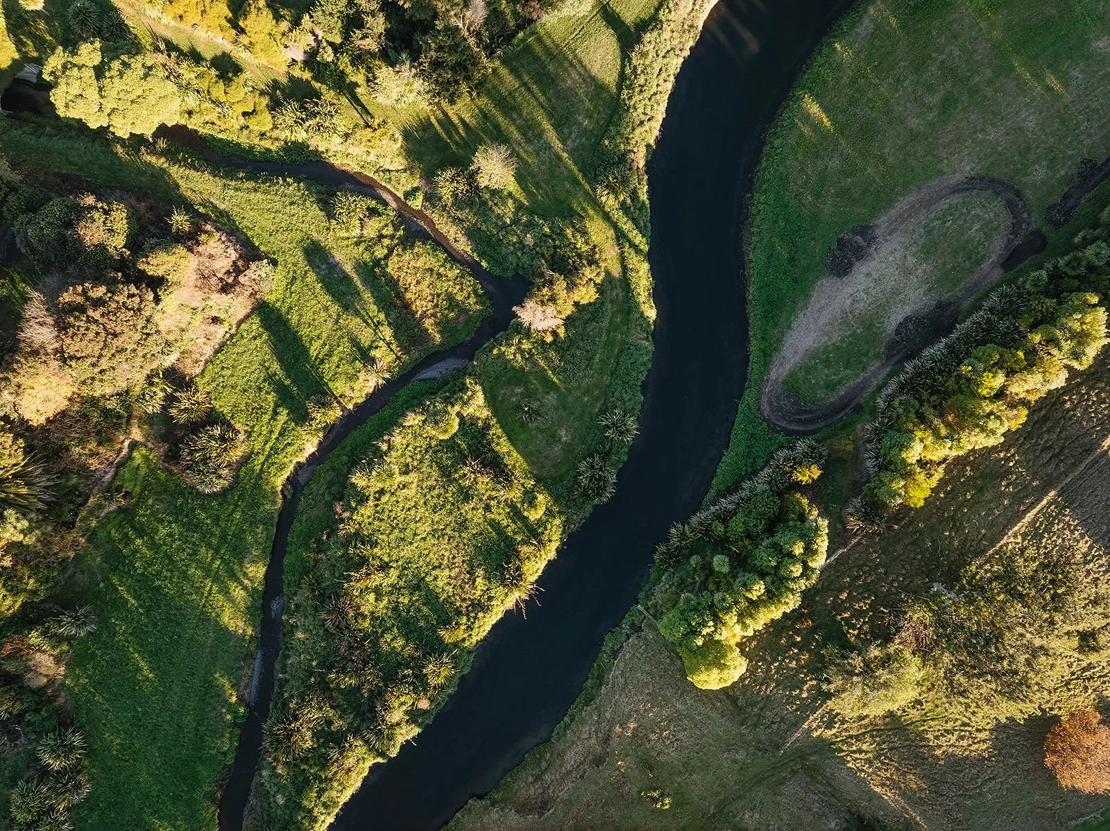 Aerial view of a river winding through a lush green landscape with trees, grass, and a small boat dock, captured during daytime.