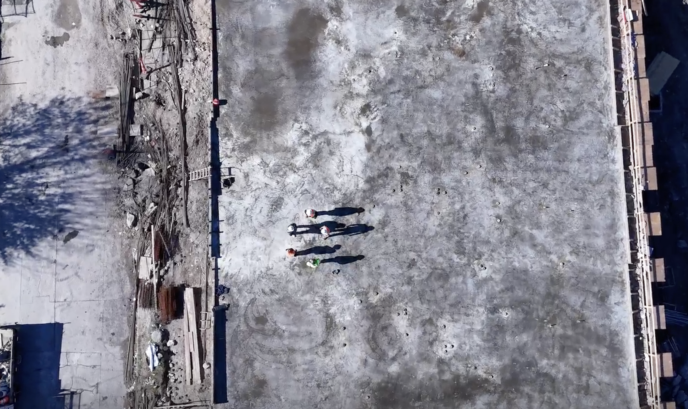 Overhead view of crew members standing on a broad concrete surface at a construction site.