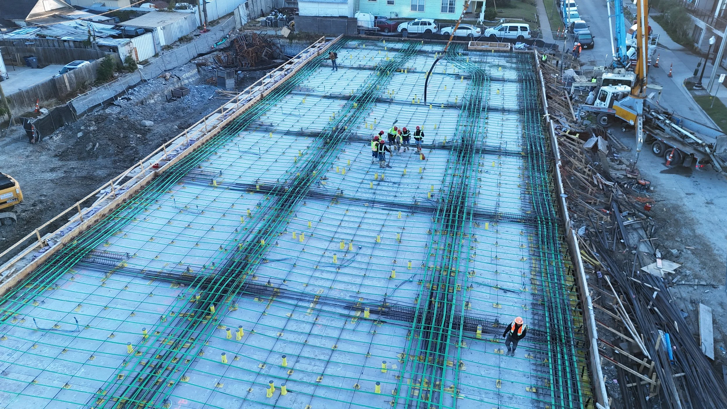Aerial view of workers among steel reinforcement grids and formwork prepared for concrete placement.