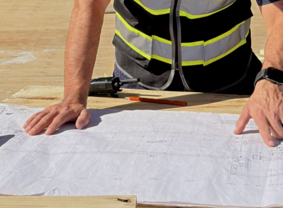 Construction professional in a reflective vest reviewing printed plans on a work table.