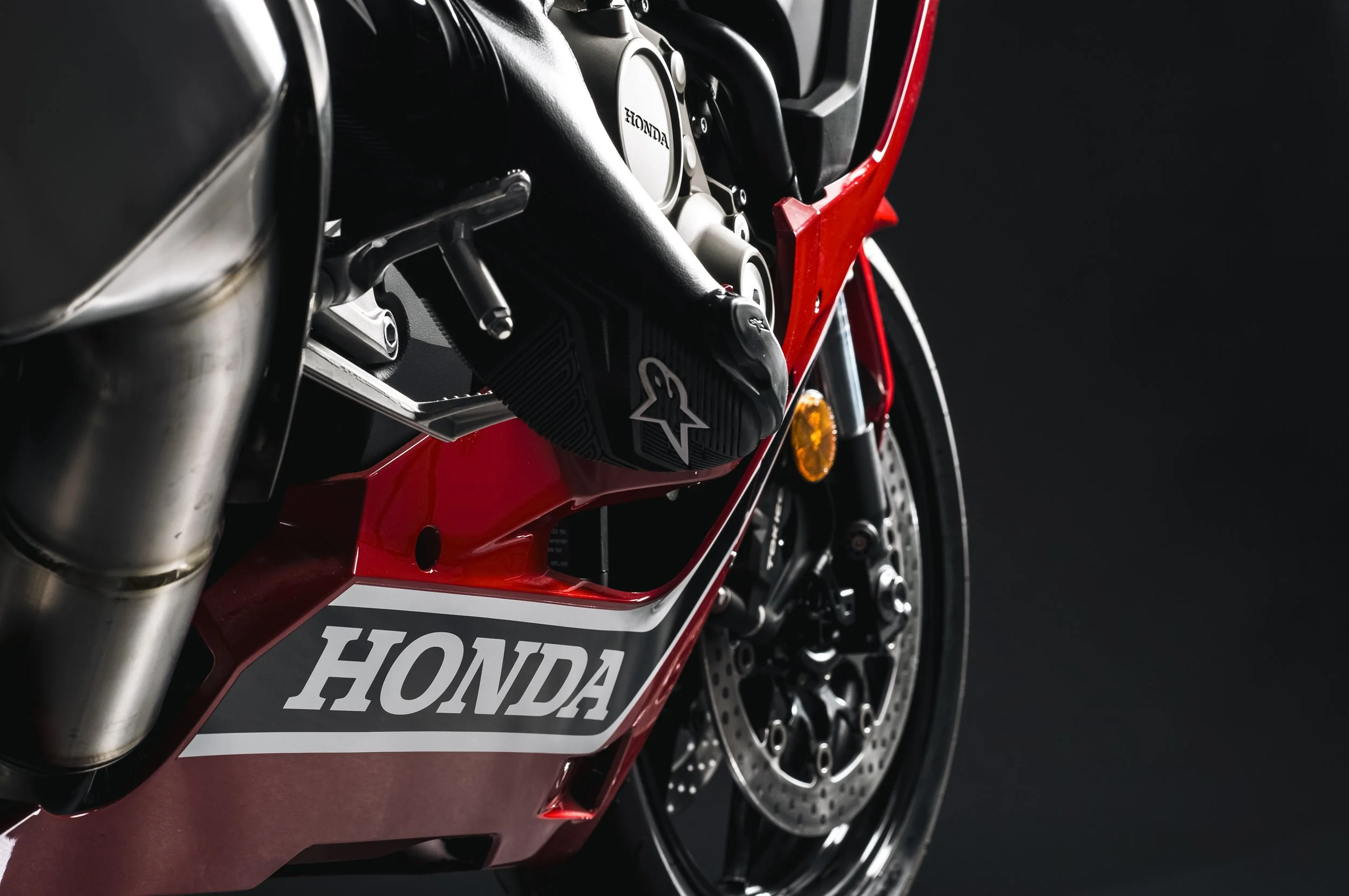 Une moto de course Honda, avec un moteur visible, un cadre rouge et des composants noirs, photographiée en gros plan.