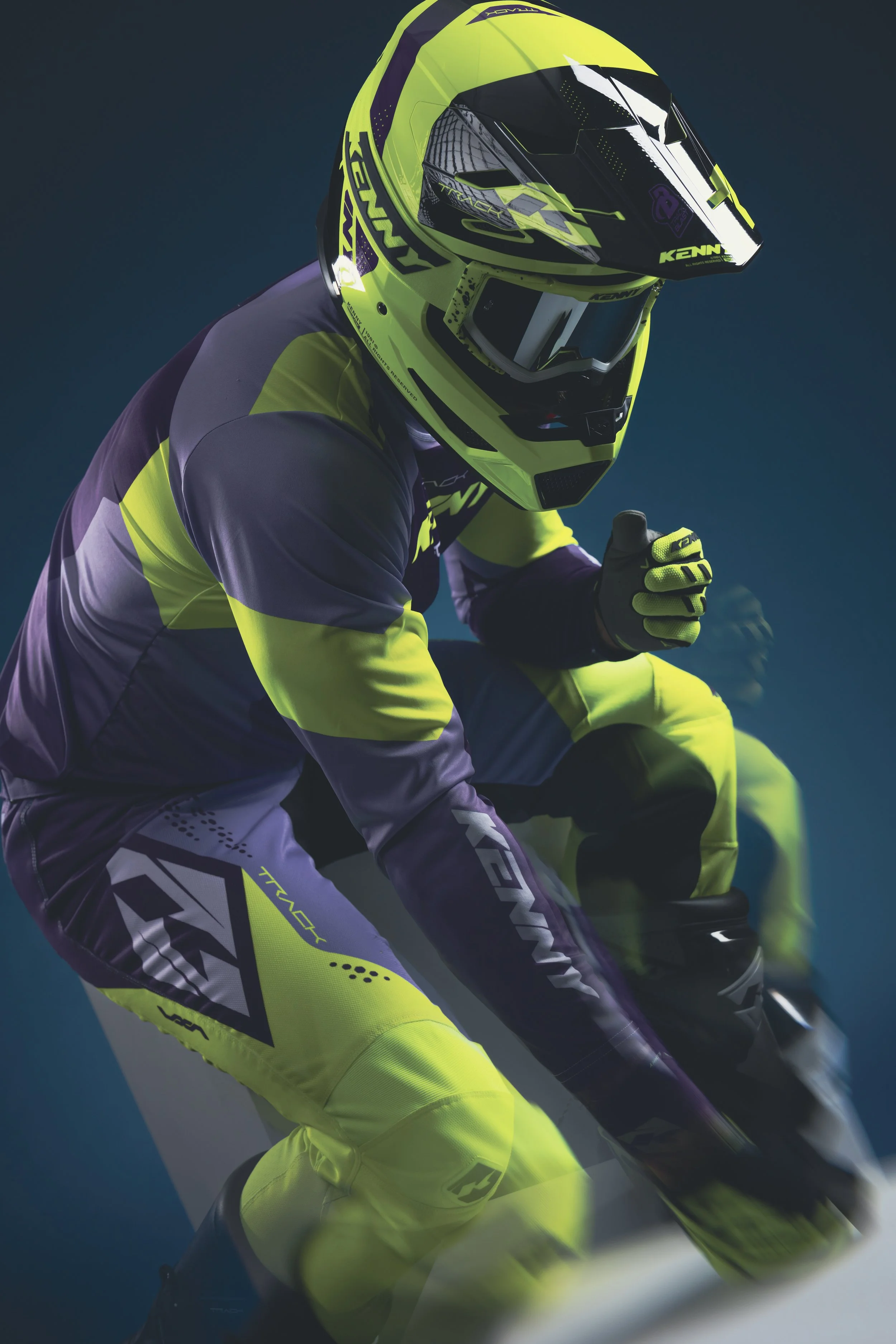 Un motocycliste en tenue de sport jaune et violet, portant un casque intégral, en position de conduite sur un vélo.