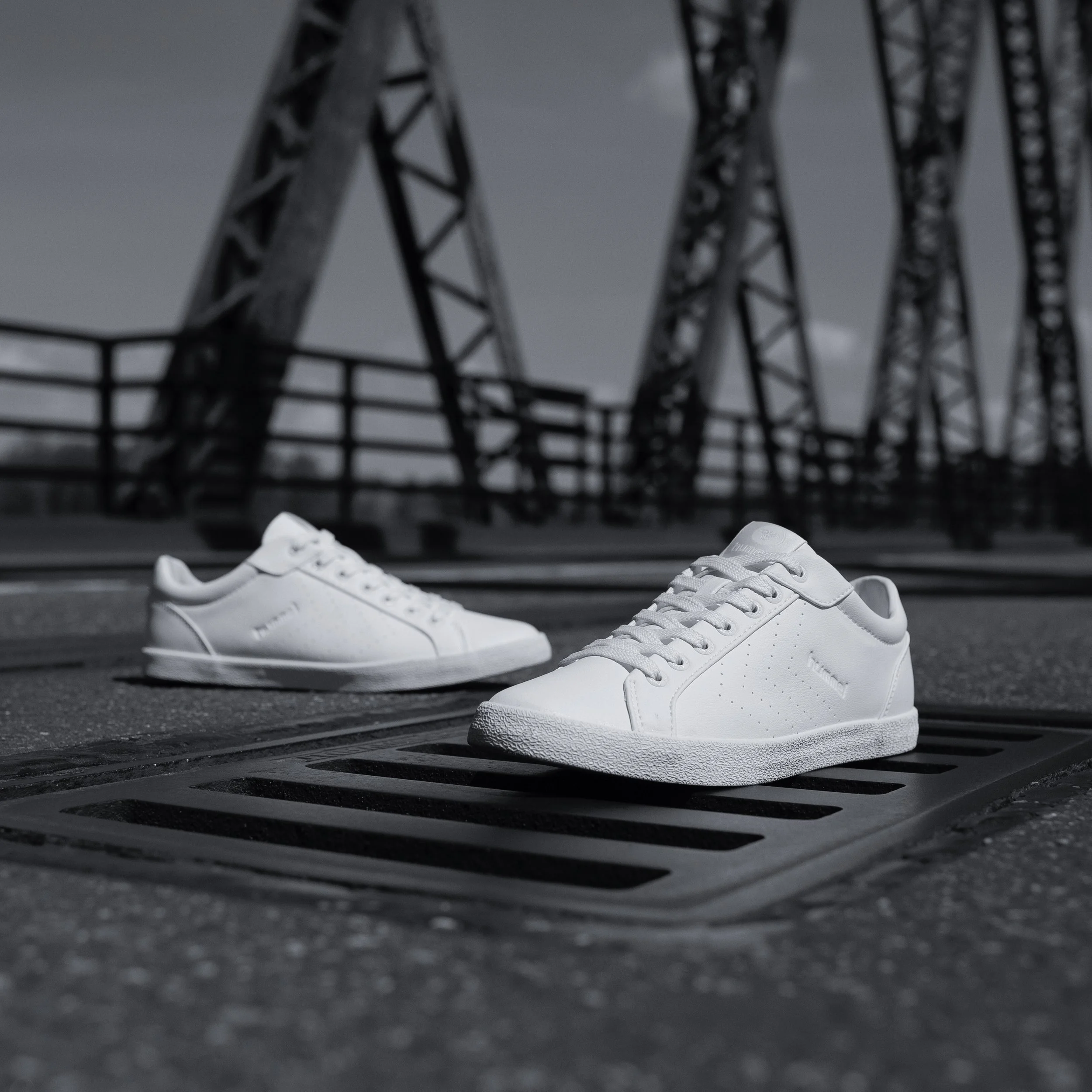 Chaussures blanches posées sur un sol noir au premier plan avec une structure métallique sombre floue en arrière-plan