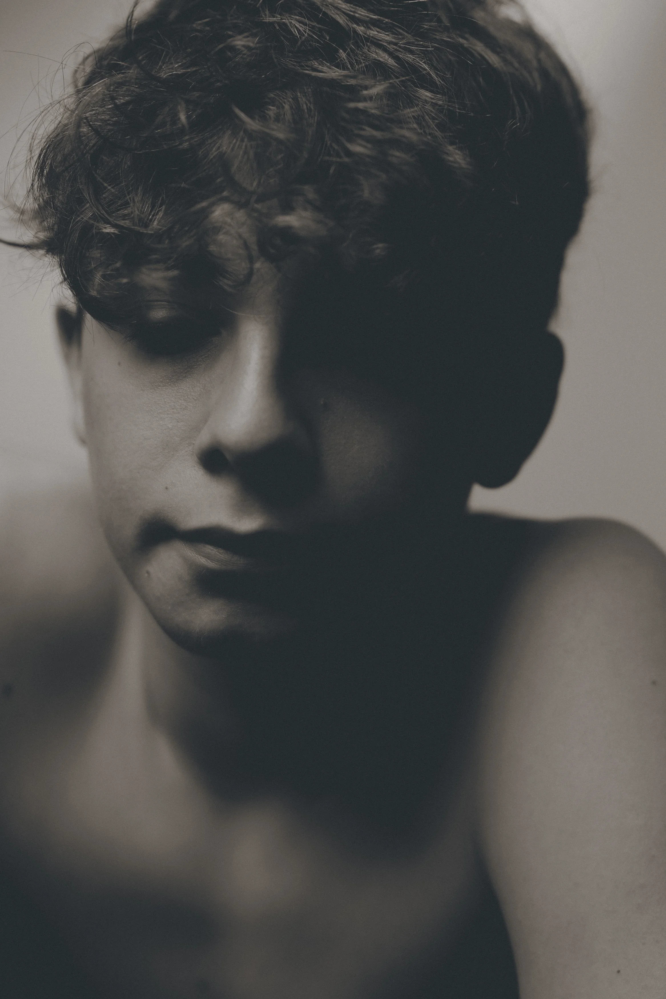 Portrait en noir et blanc d'une personne avec des cheveux bouclés, regardant vers le bas, avec une expression sérieuse.