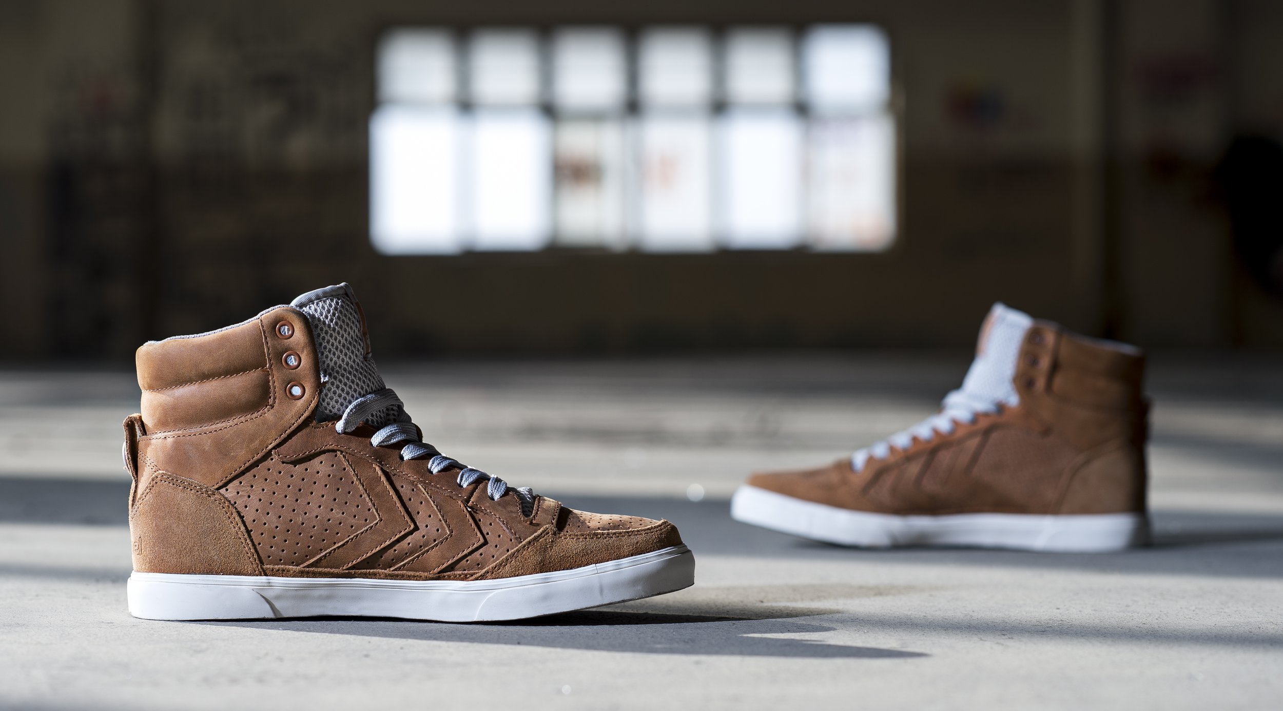 Une paire de baskets en cuir marron posée au sol dans une pièce avec une grande fenêtre en arrière-plan.
