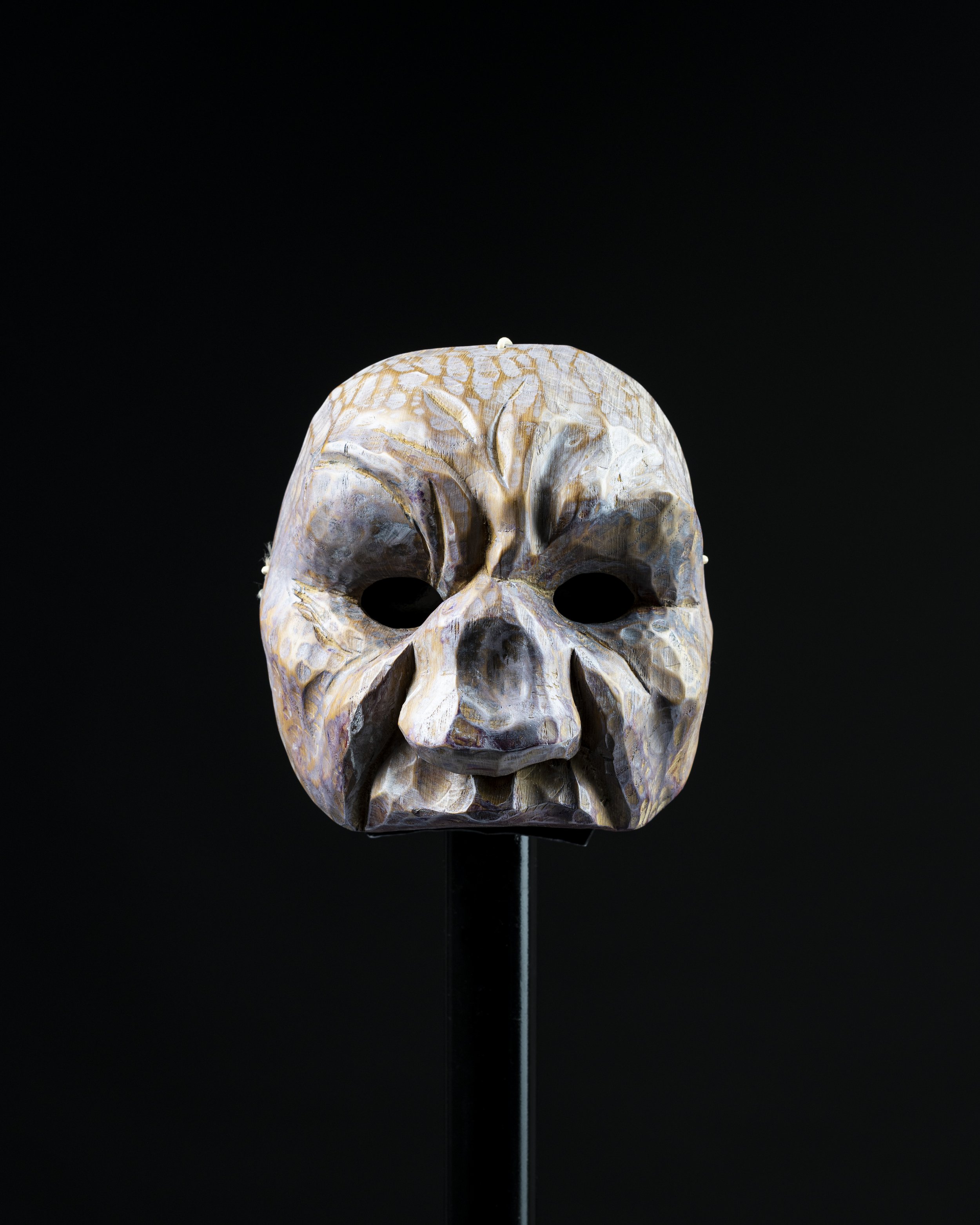 Masque en forme de crâne humain, ancien, en pierre ou en os, exposé sur fond noir.