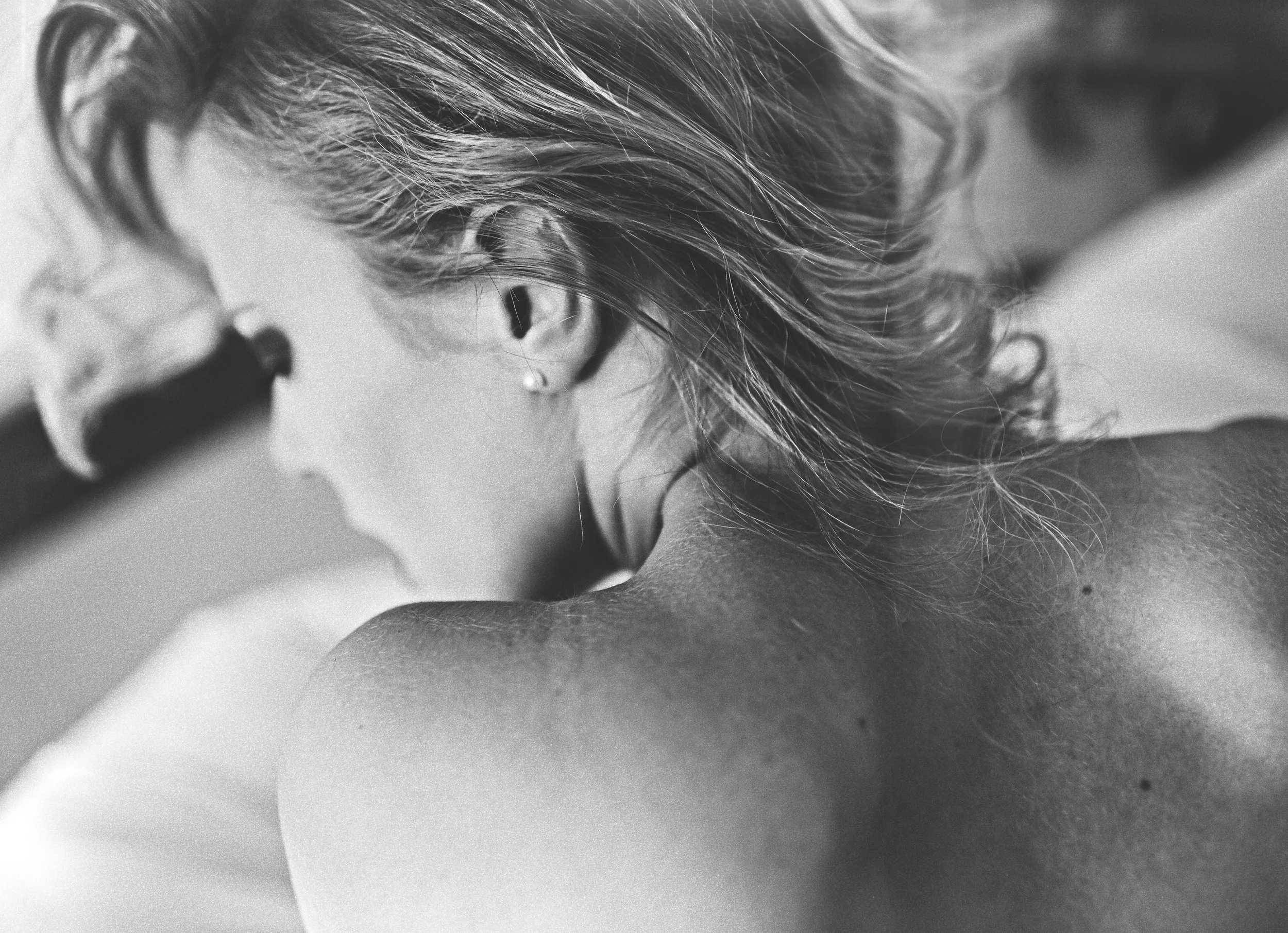 Photo en noir et blanc d'une personne avec des cheveux courts, vue de dos, en train d'utiliser un microscope.