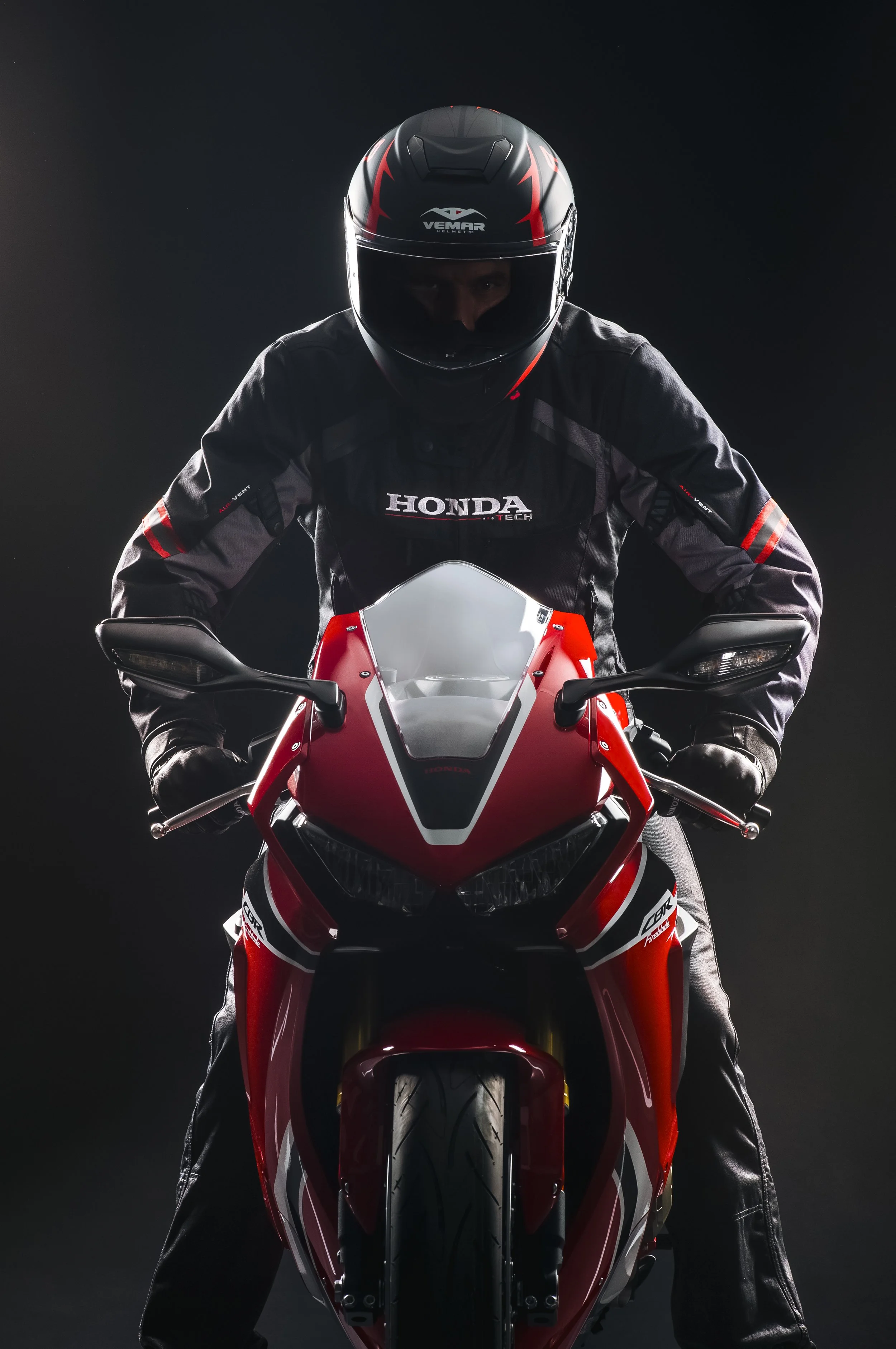 Un pilote en tenue de course et casque, assis sur une moto Honda de sport, dans un environnement sombre.