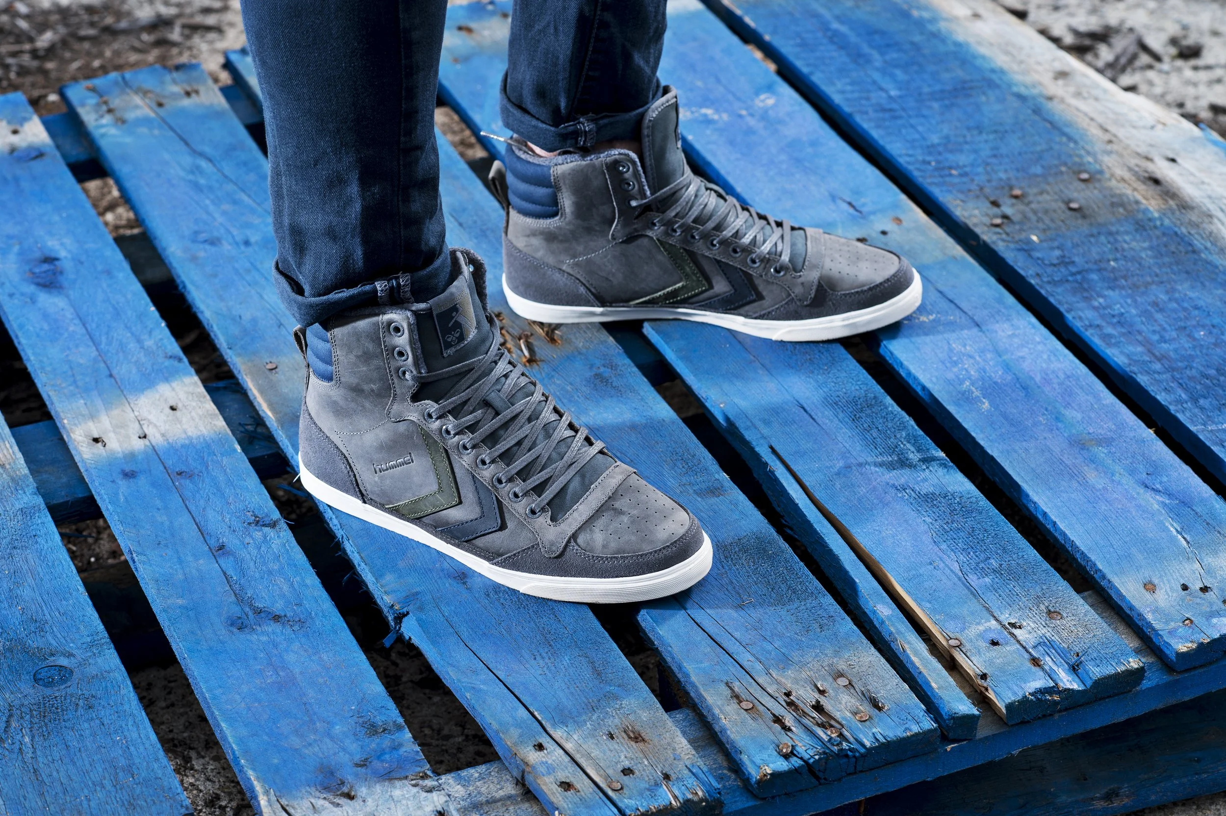 Chaussures de sport grises et noires portées par une personne debout sur un pont en bois peint en bleu, en extérieur.