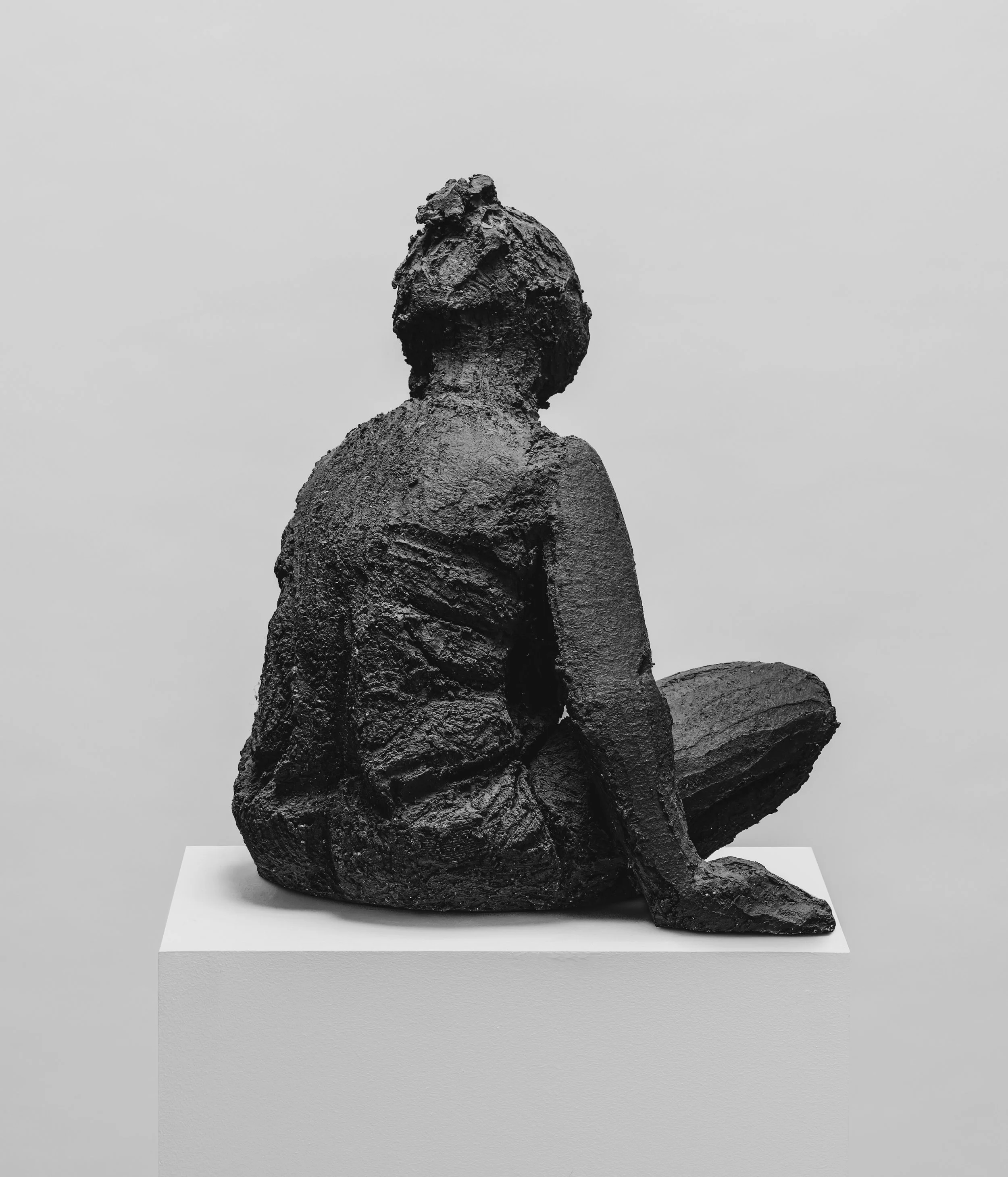 Sculpture abstraite en bronze, représentant une figure humaine stylisée, exposée sur un socle blanc dans une galerie d'art.