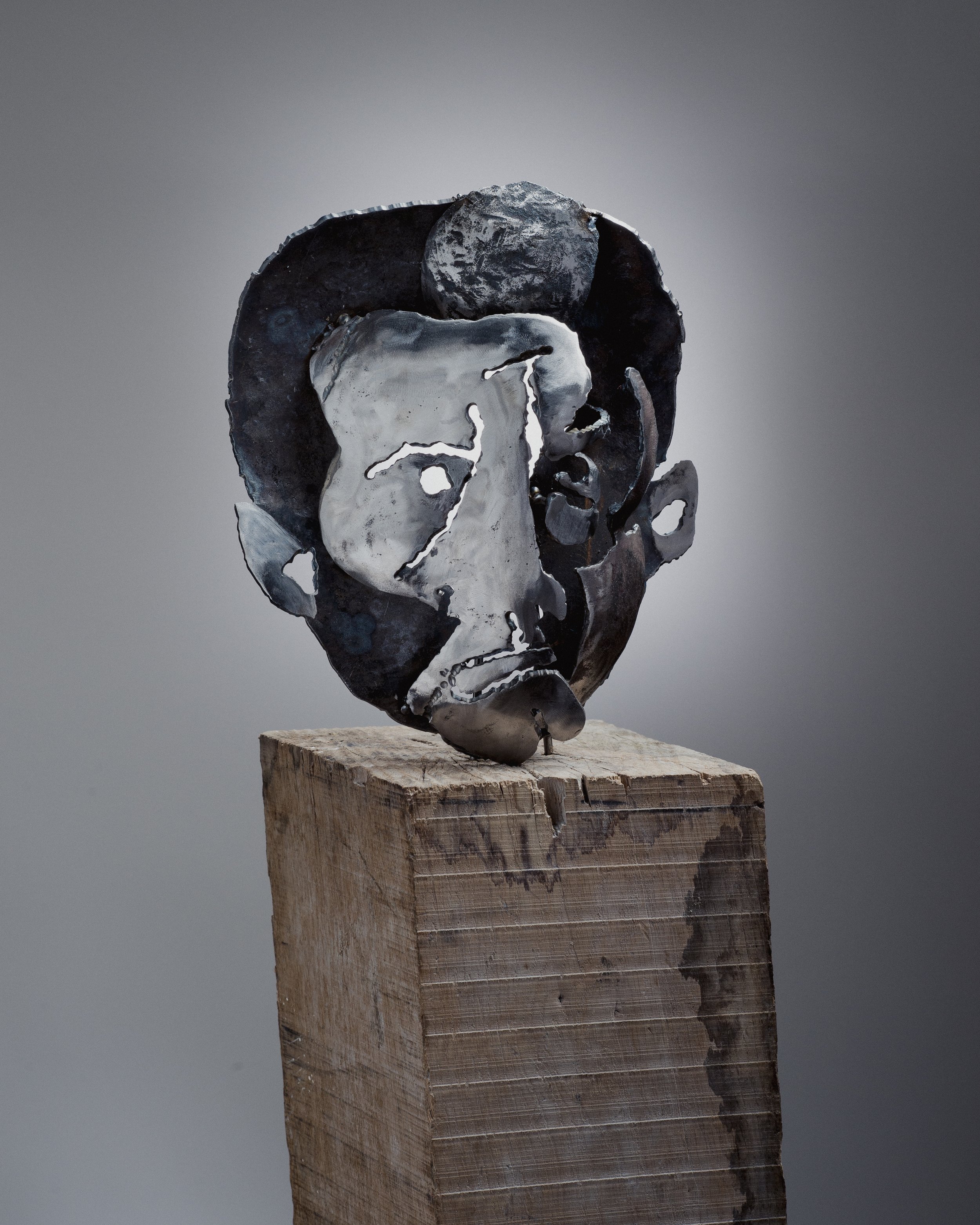Sculpture moderne représentant une tête humaine en métal, posée sur une base en bois.