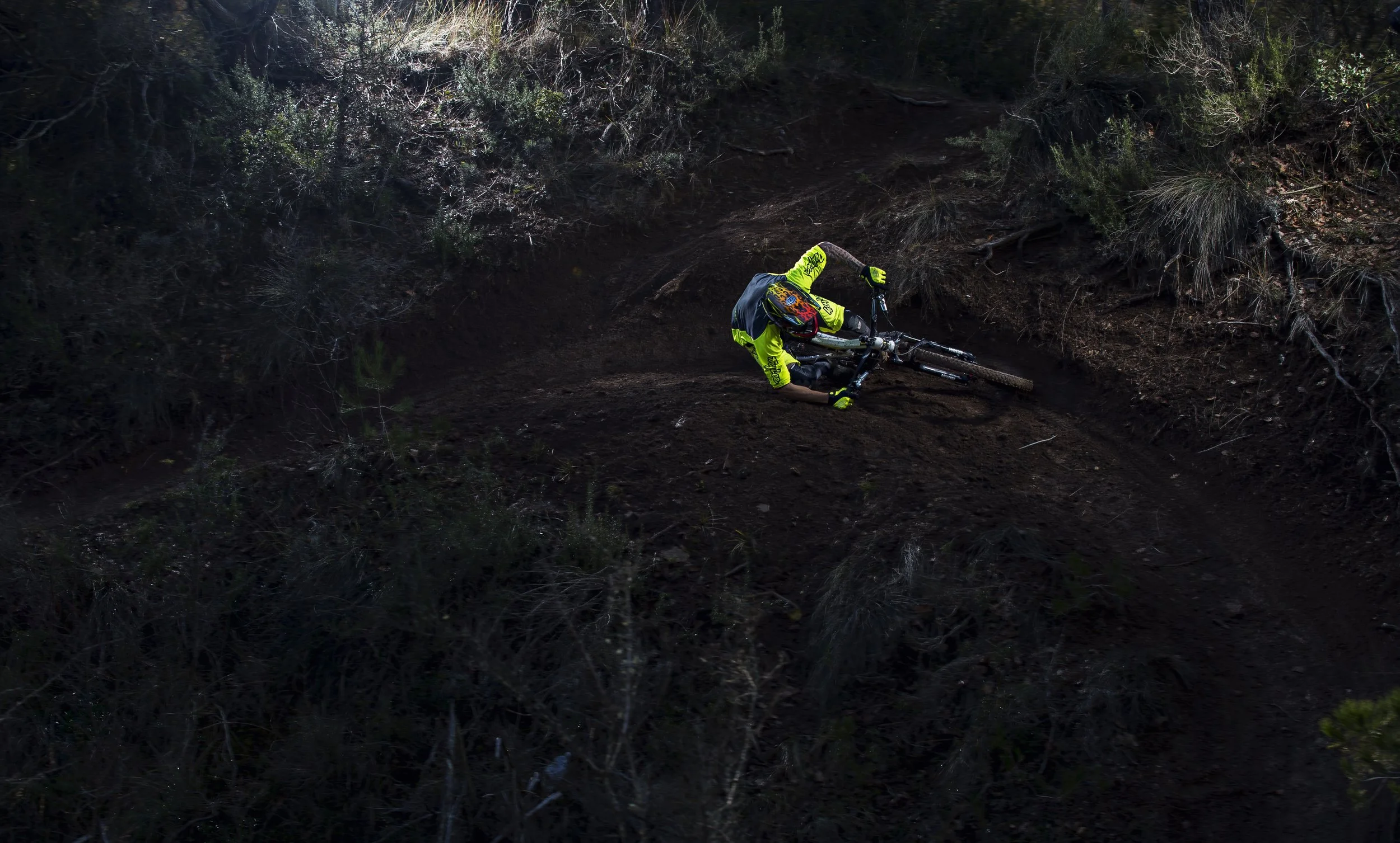 VTT tombé sur un sentier en terre dans une forêt, vue de côté avec le cycliste écarté du centre, se trouvant en position allongée avec le vélo à côté.