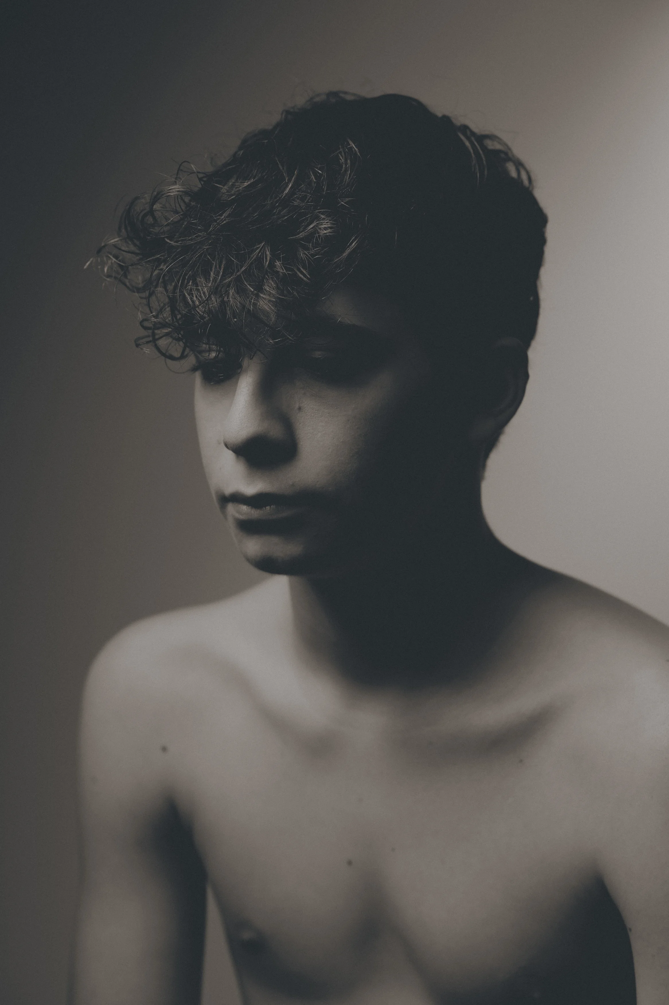Portrait en noir et blanc d'une femme nue avec des cheveux bouclés, regardant vers le bas.