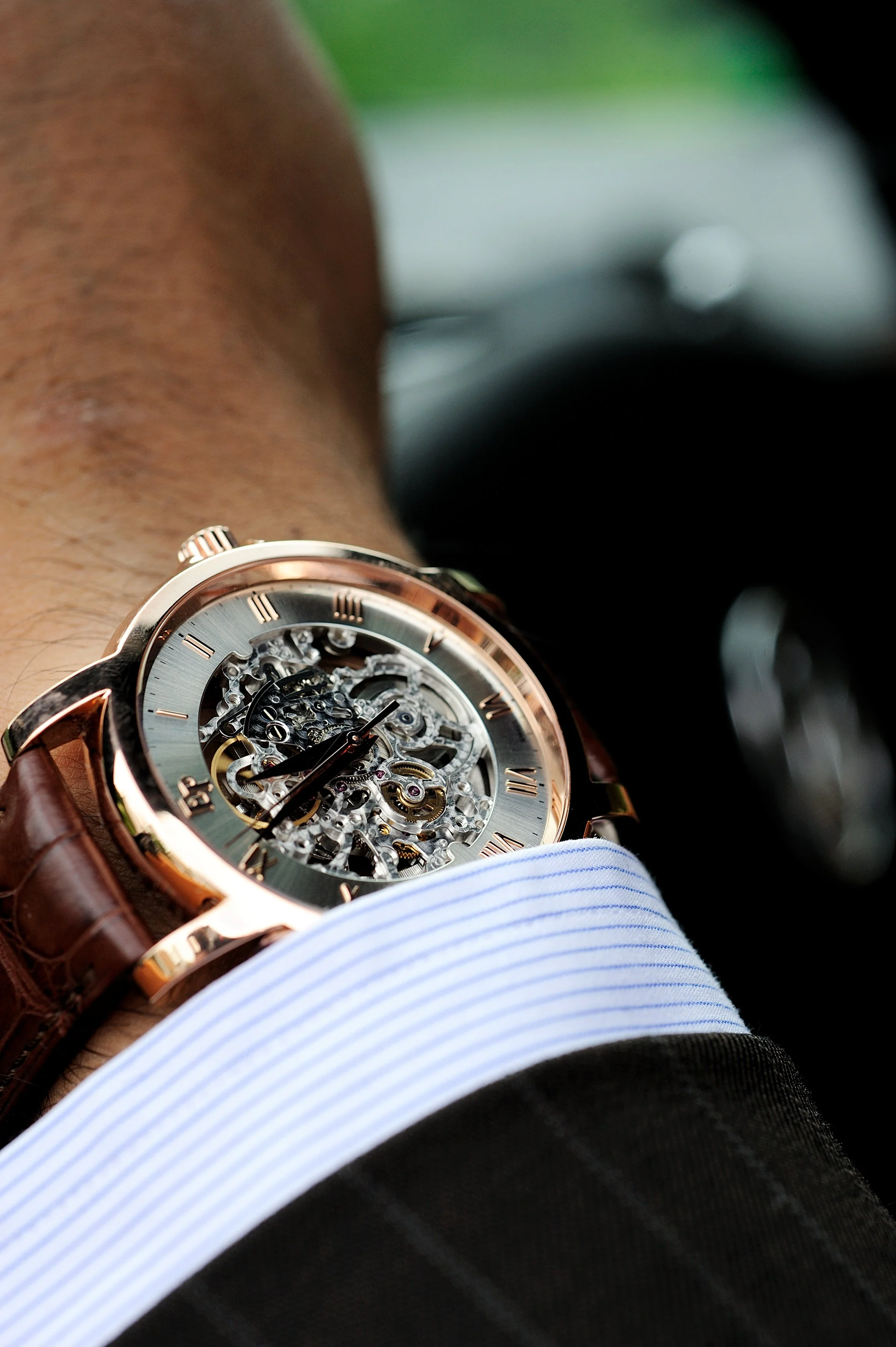Montre-bracelet avec un mécanisme squelette visible sur le poignet d'une personne habillée en chemise à rayures bleues et blanches.