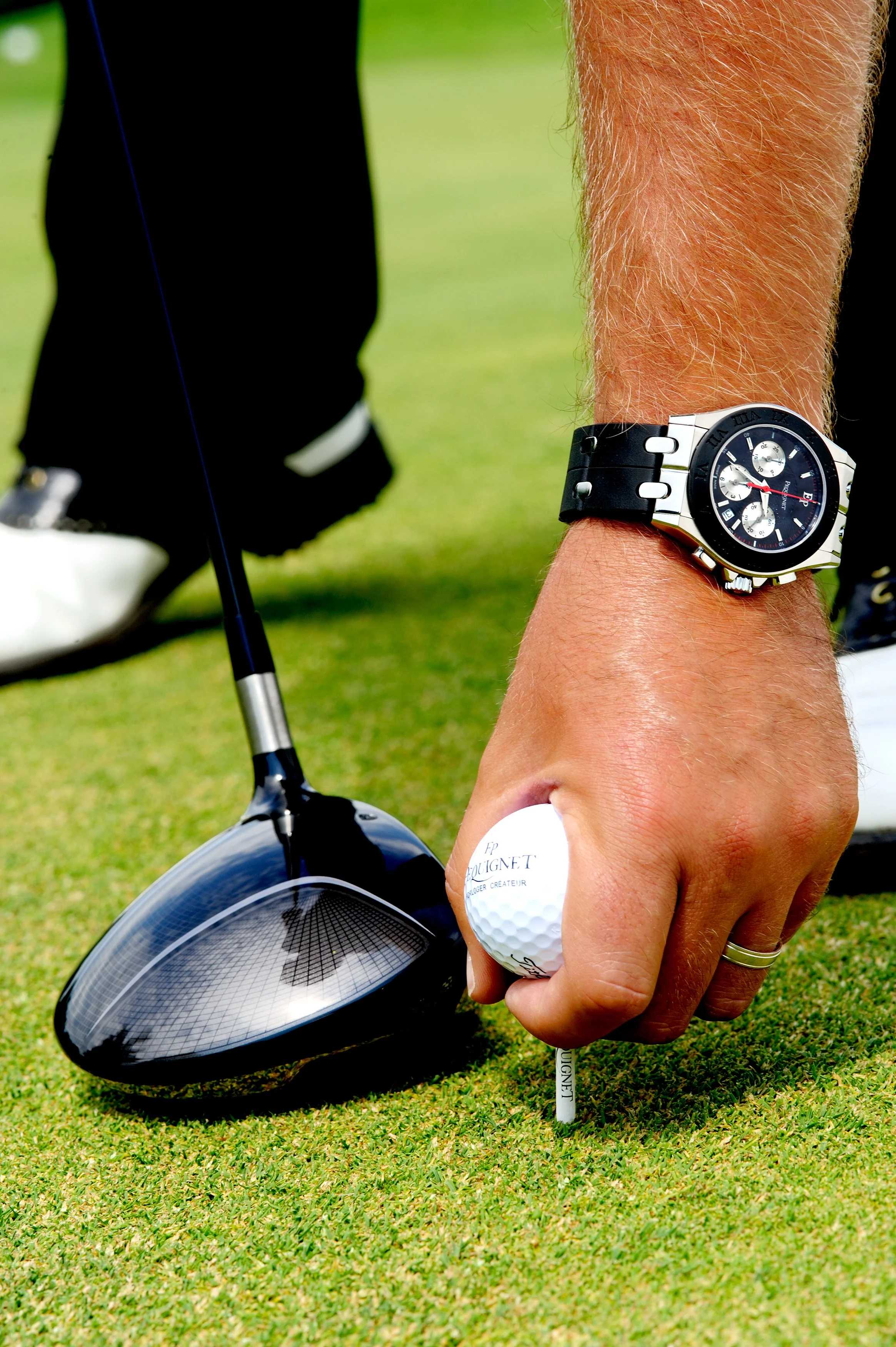 Une main tenant une balle de golf à côté d'un club de golf sur une surface de gazon.