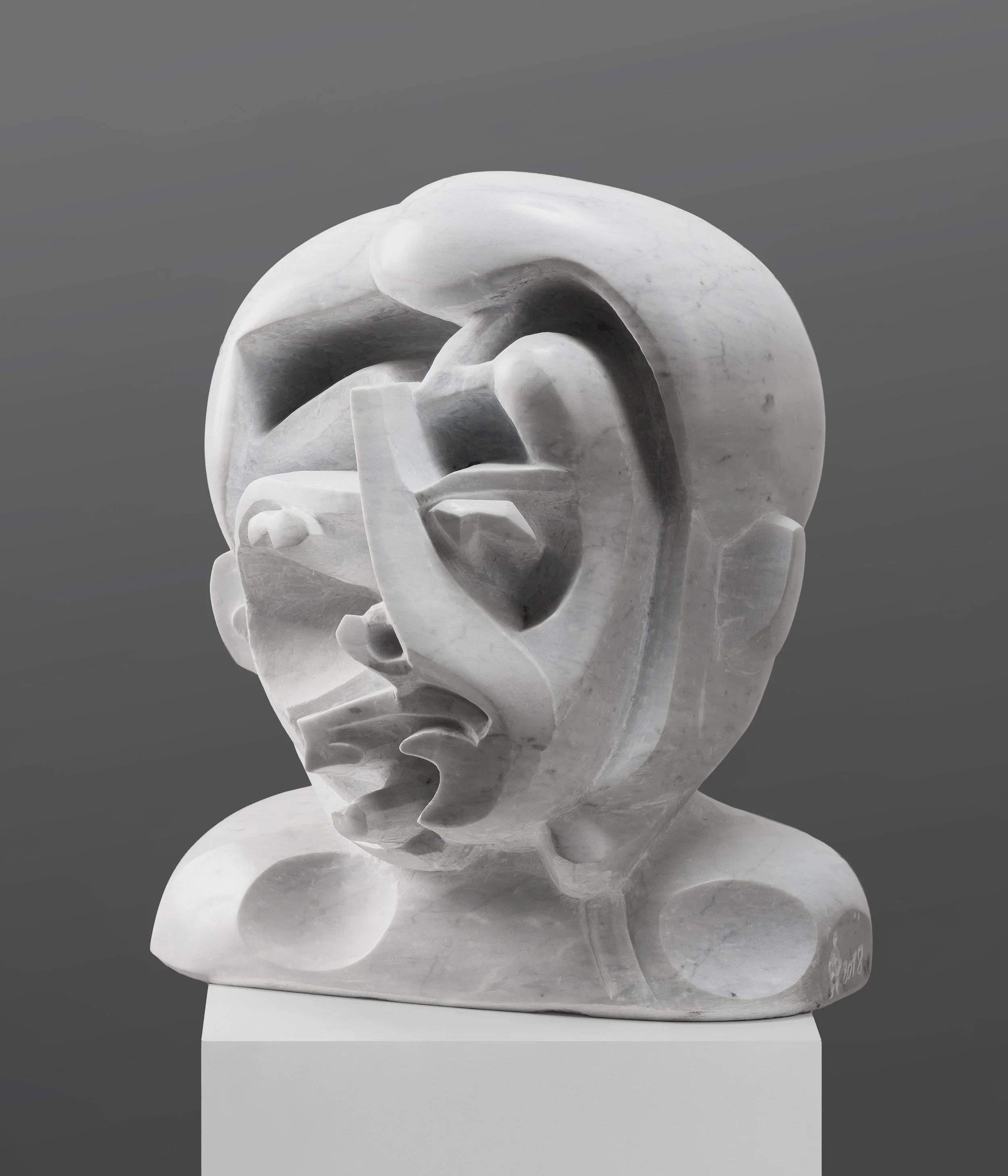 Sculpture en marbre blanc représentant un visage humain stylisé, avec des formes abstraites et fluides, sur une base blanche.