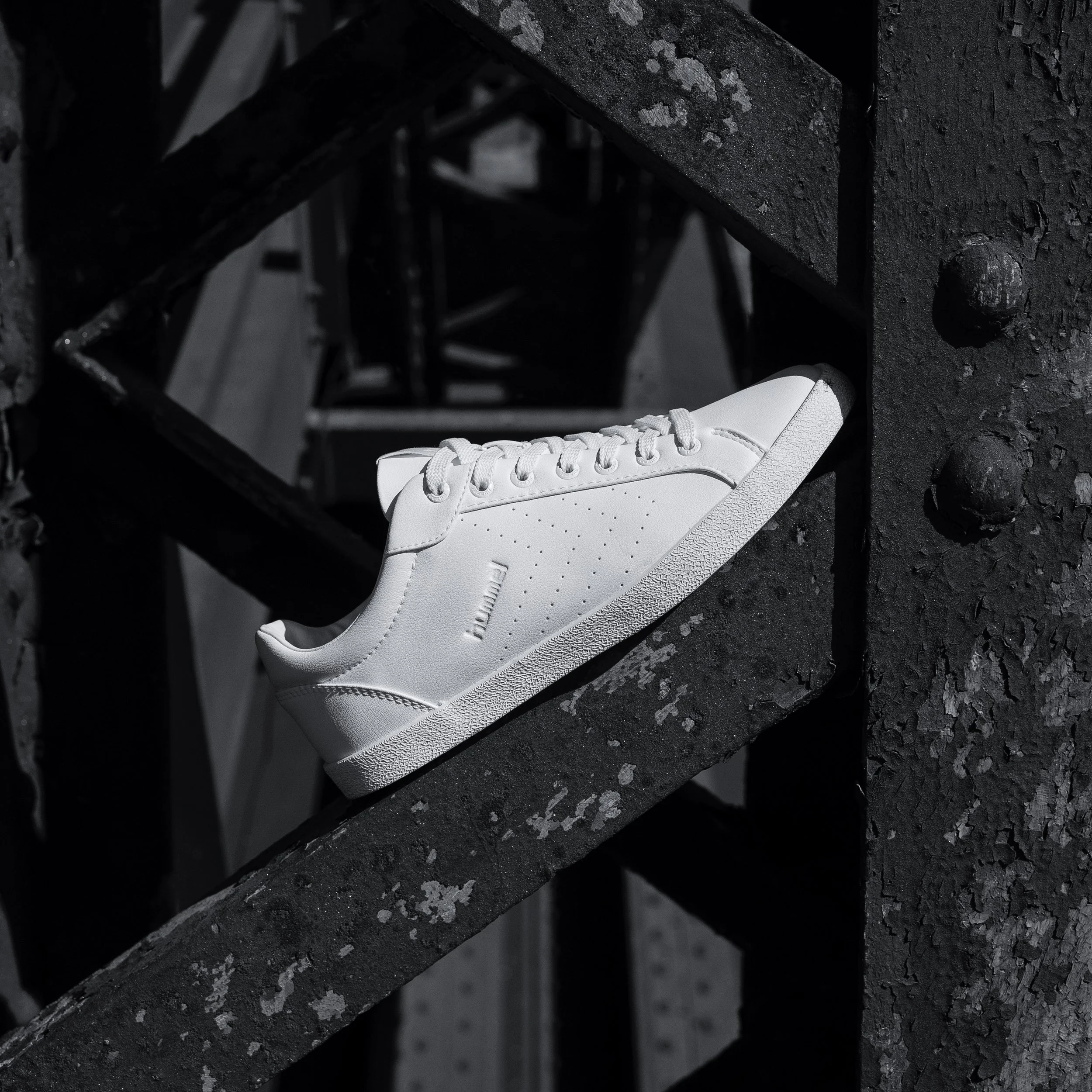 Chaussure blanche sur un sol noir avec des textures granulaires dans une ambiance sombre.