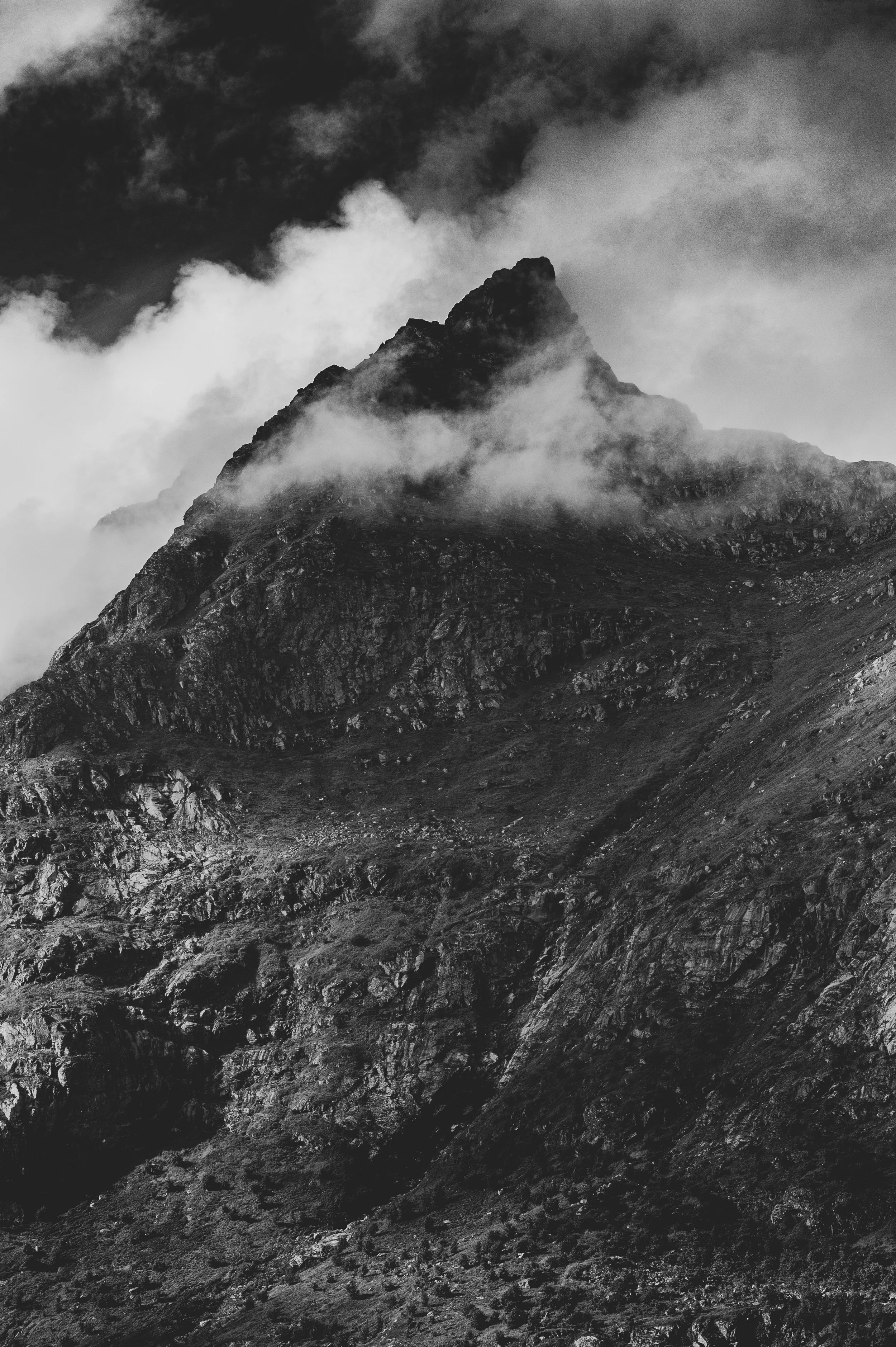 Montagne rocheuse avec des nuages environnants en noir et blanc.