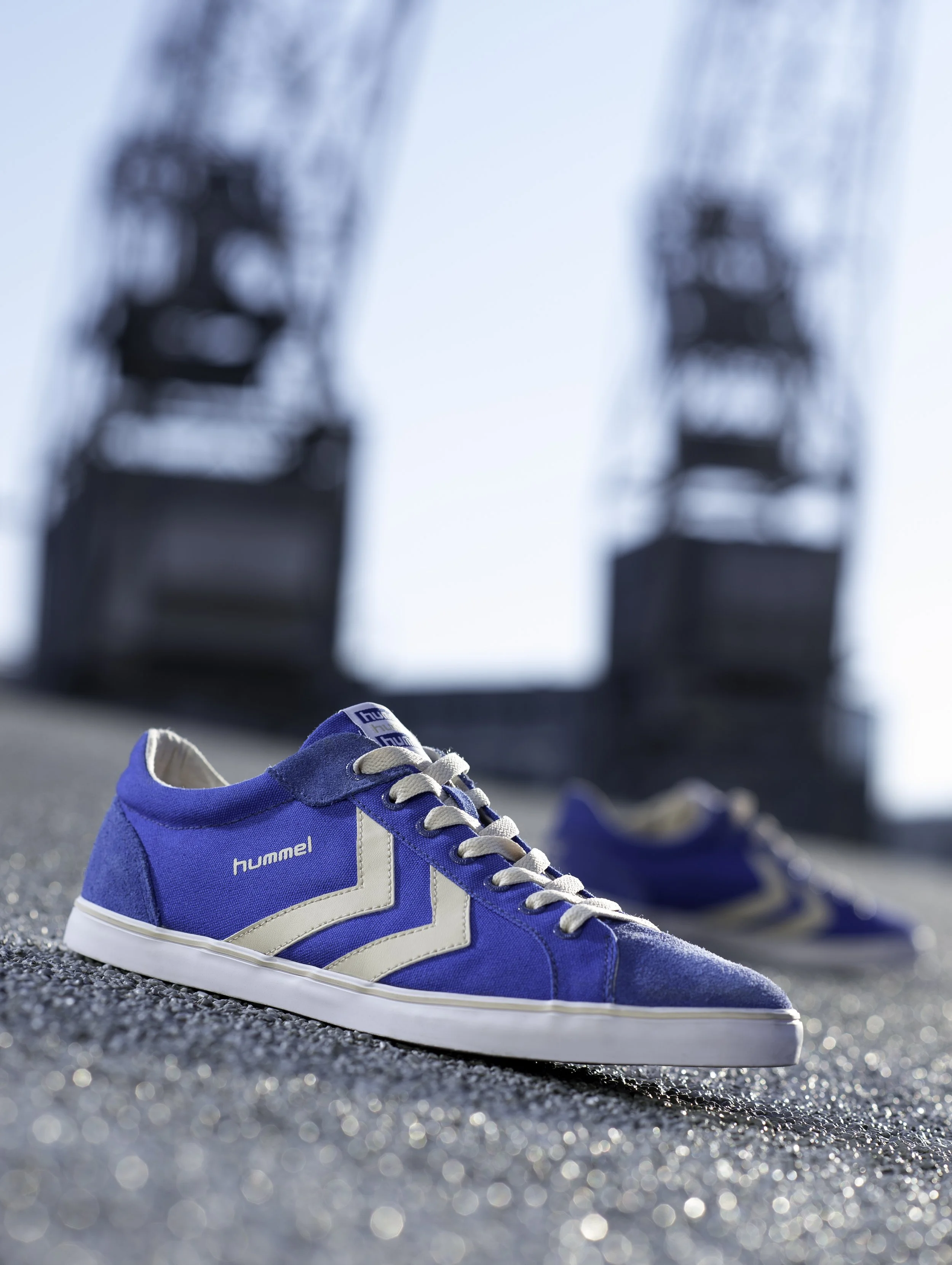 Une paire de chaussures de sport bleues sur un sol pavé, avec un arrière-plan flou de deux structures