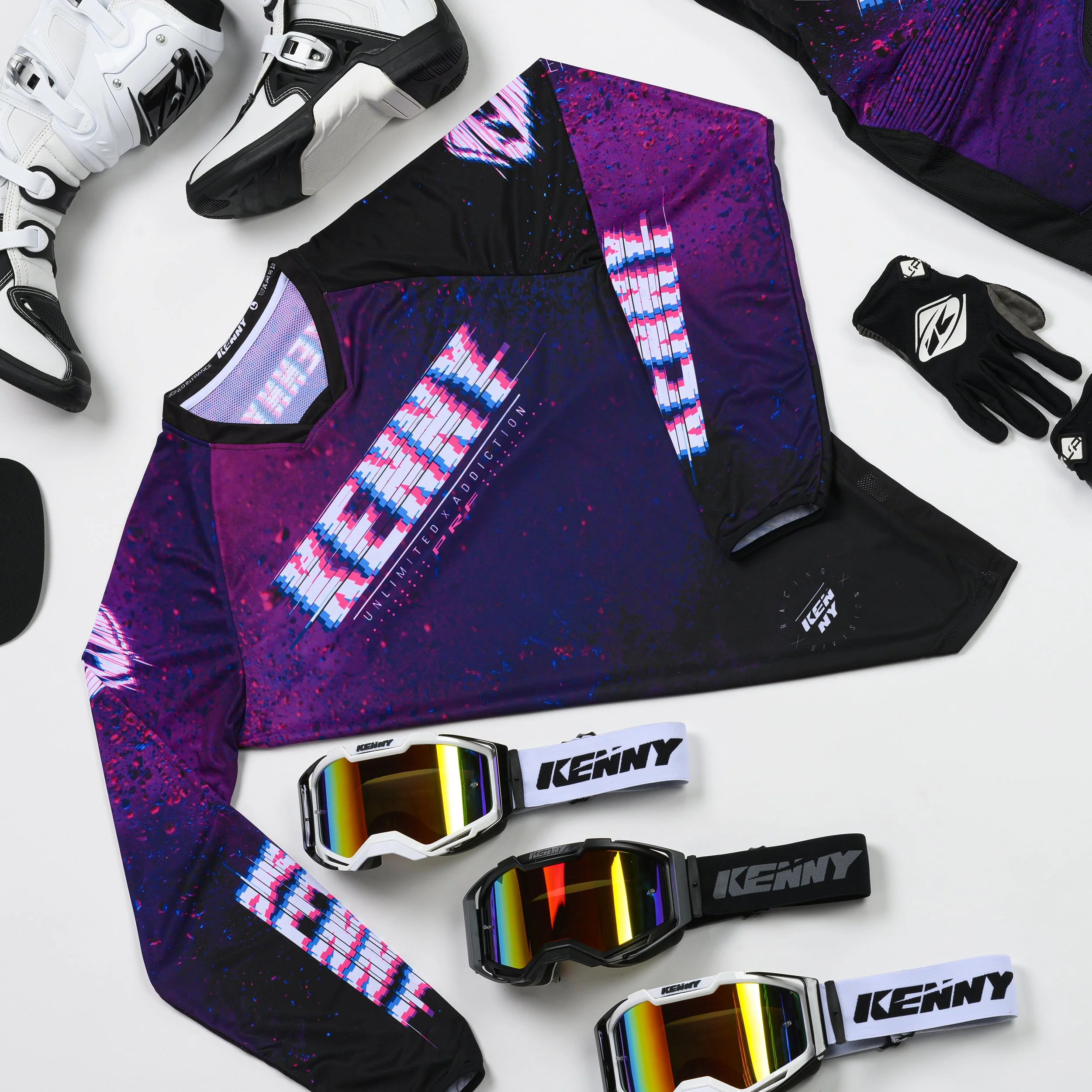 Équipement de motocross avec casque, masque, gants, et vêtements colorés à motifs violets et noirs, disposés sur une surface blanche.
