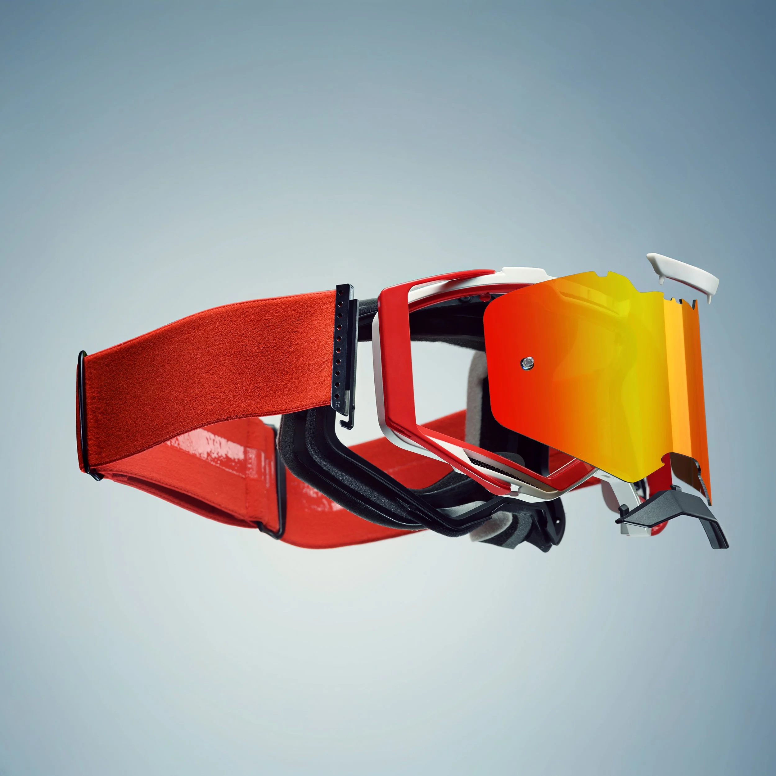 Une composition d’accessoires de sport, notamment des lunettes de protection jaune, des casques de ski rouge et blanc, et une manchette en tissu rouge, disposés contre un fond gris clair.