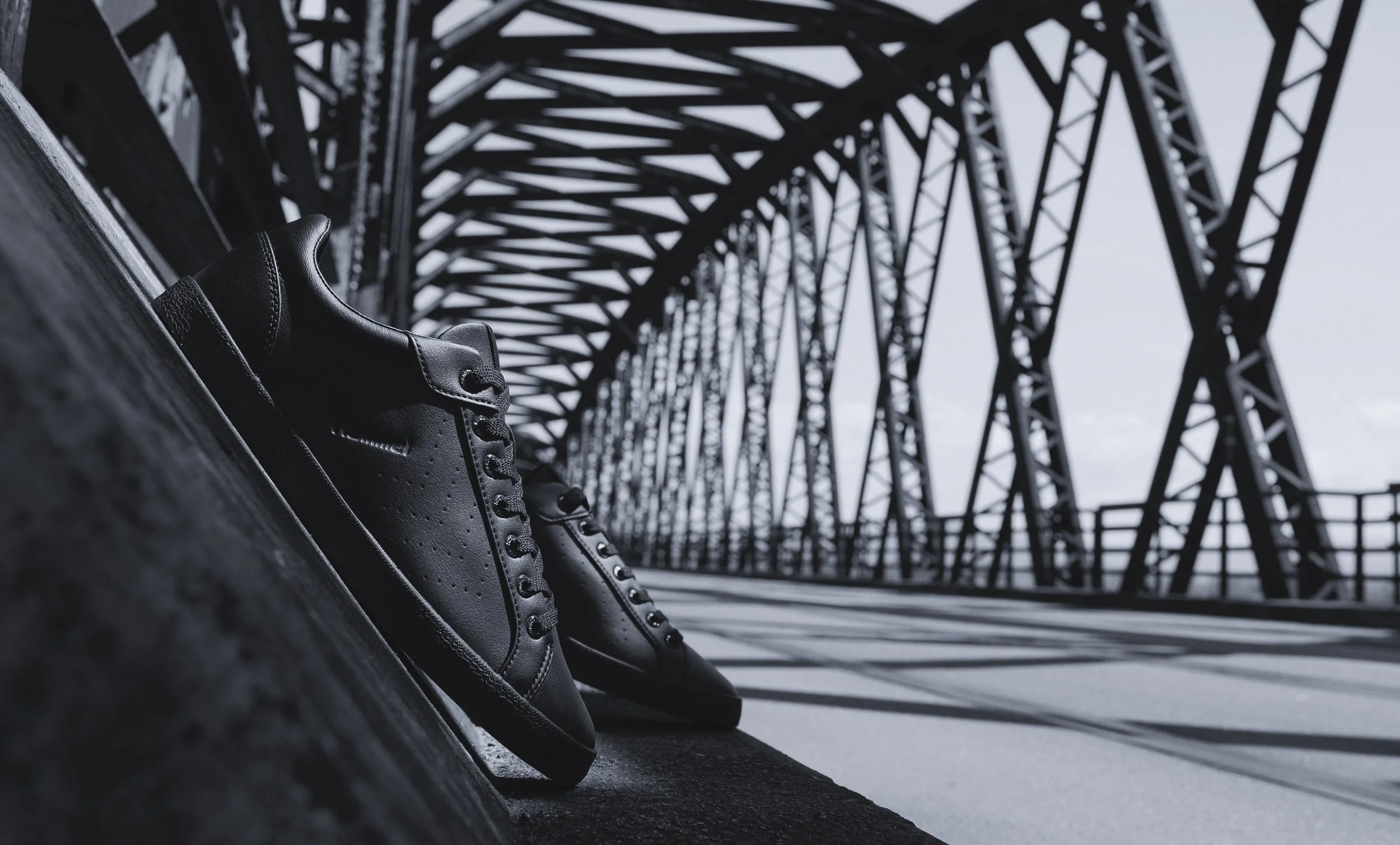 Une paire de chaussures noires en cuir posée sur le sol sous un pont métallique en acier.
