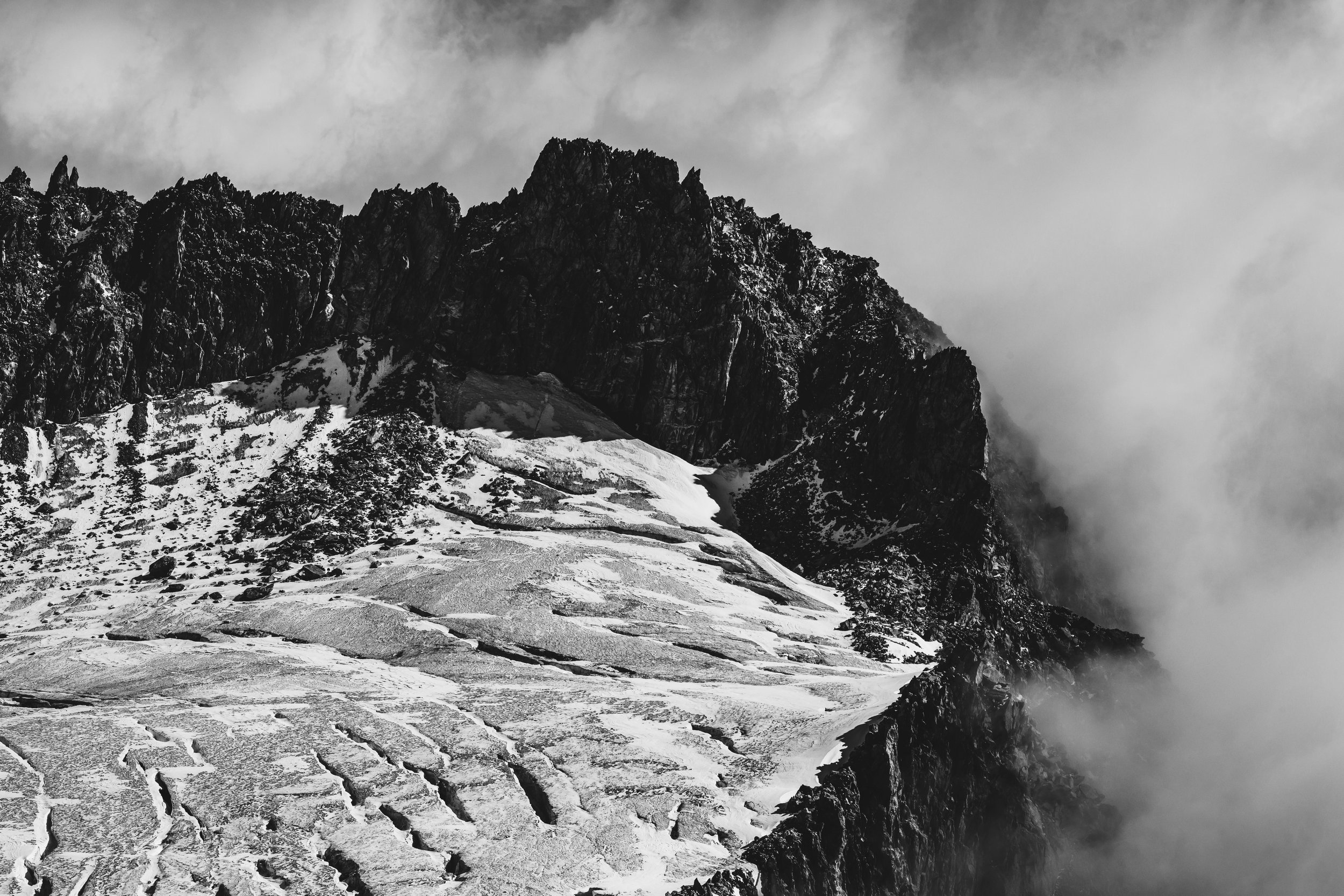 Montagnes rocheuses enneigées avec nuages et brume.