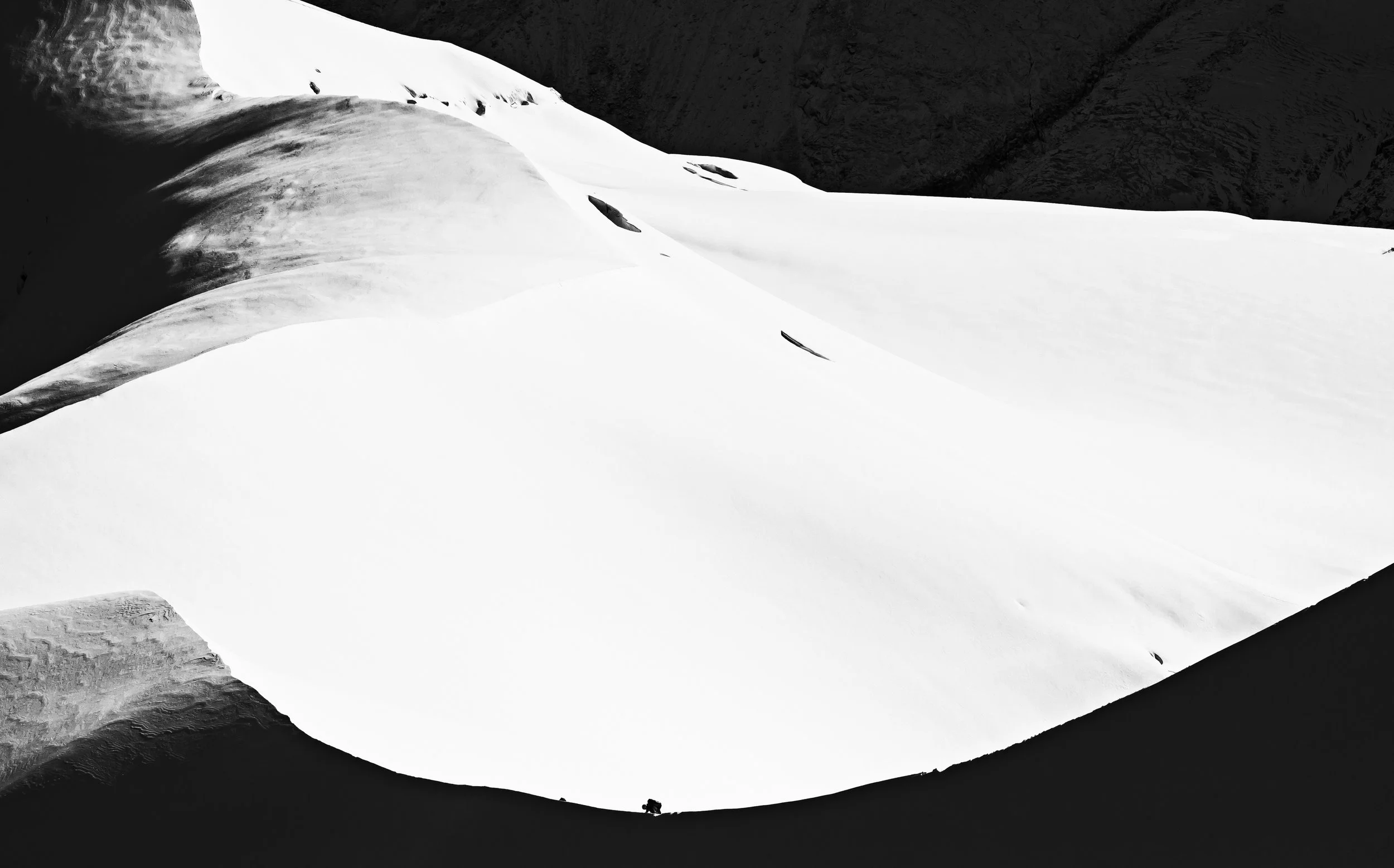 Une vue en noir et blanc d'une falaise enneigée avec un contraste marqué entre la neige blanche et la roche sombre en arrière-plan.