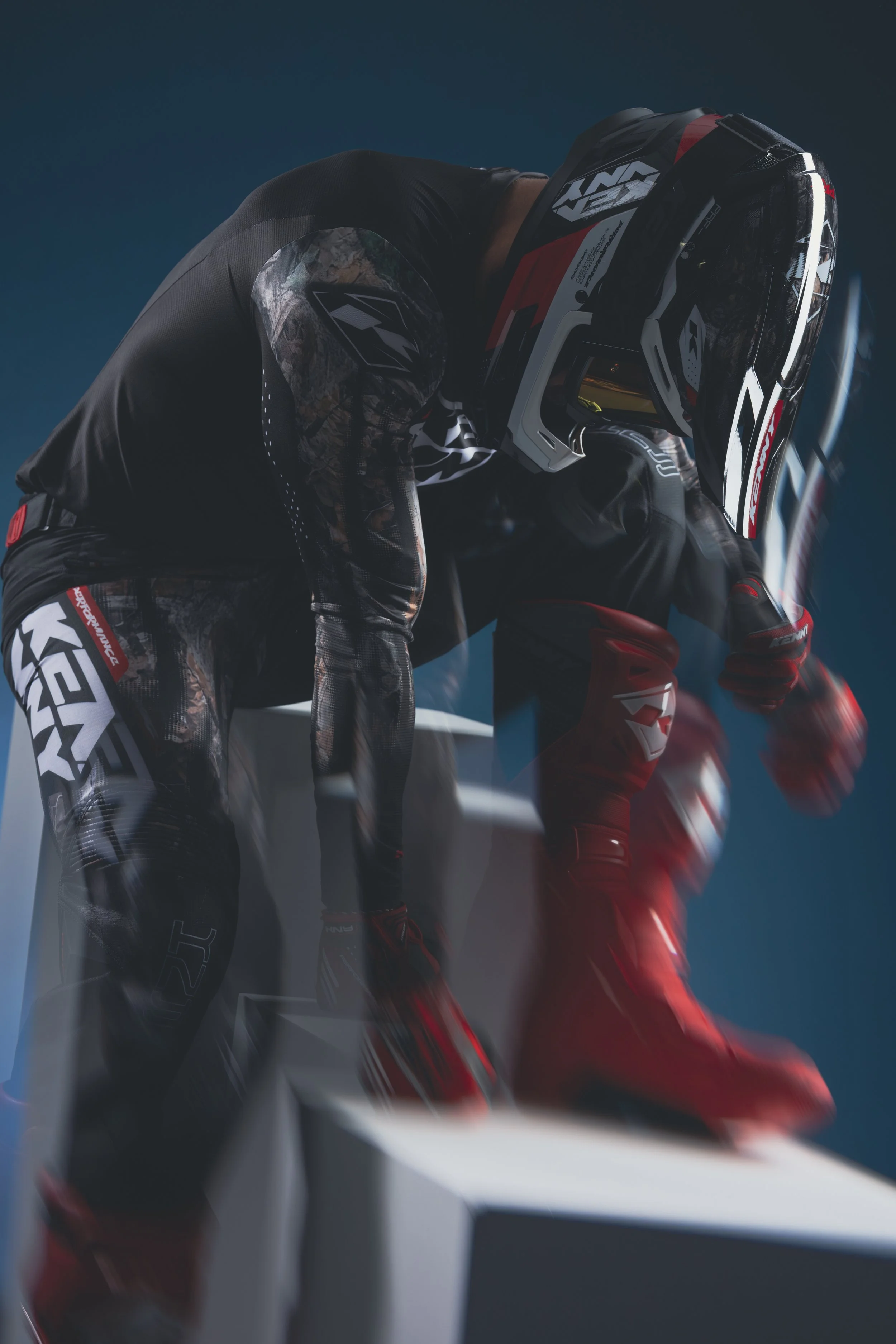 Coureurs de motocross portant des équipements de protection, dont casques, en position sur la ligne de départ dans un environnement intérieur.