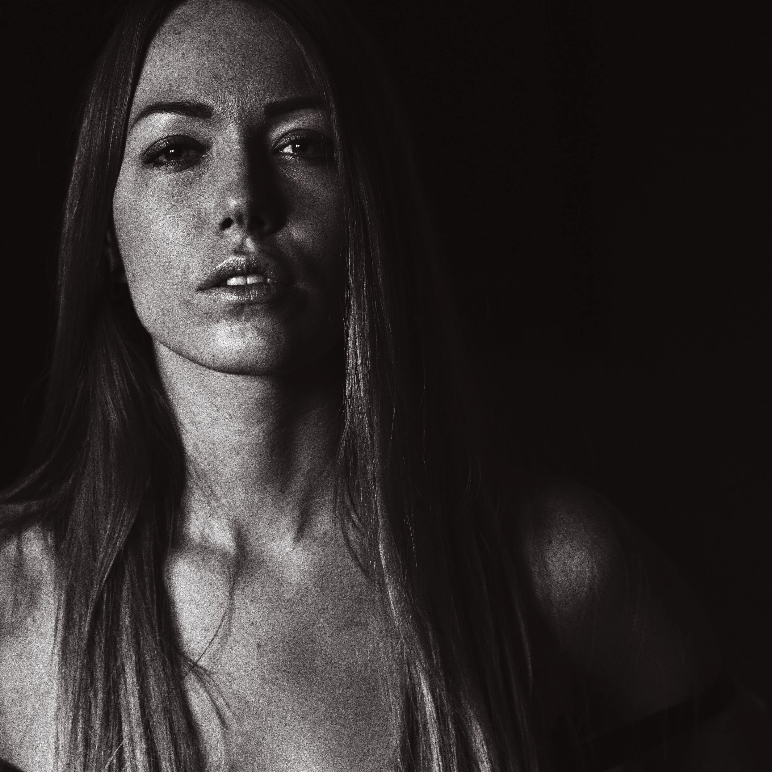 Portrait noir et blanc d'une femme avec des cheveux longs, expression neutre, fond sombre.