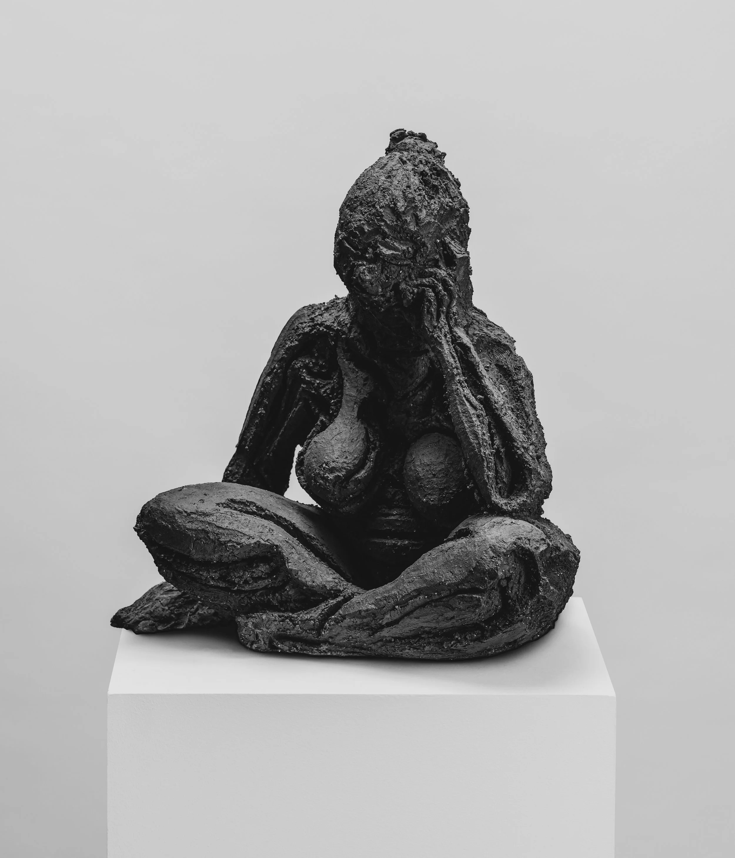 Sculpture en bronze représentant un personnage humanoïde assis, exposée sur un socle blanc dans un musée.
