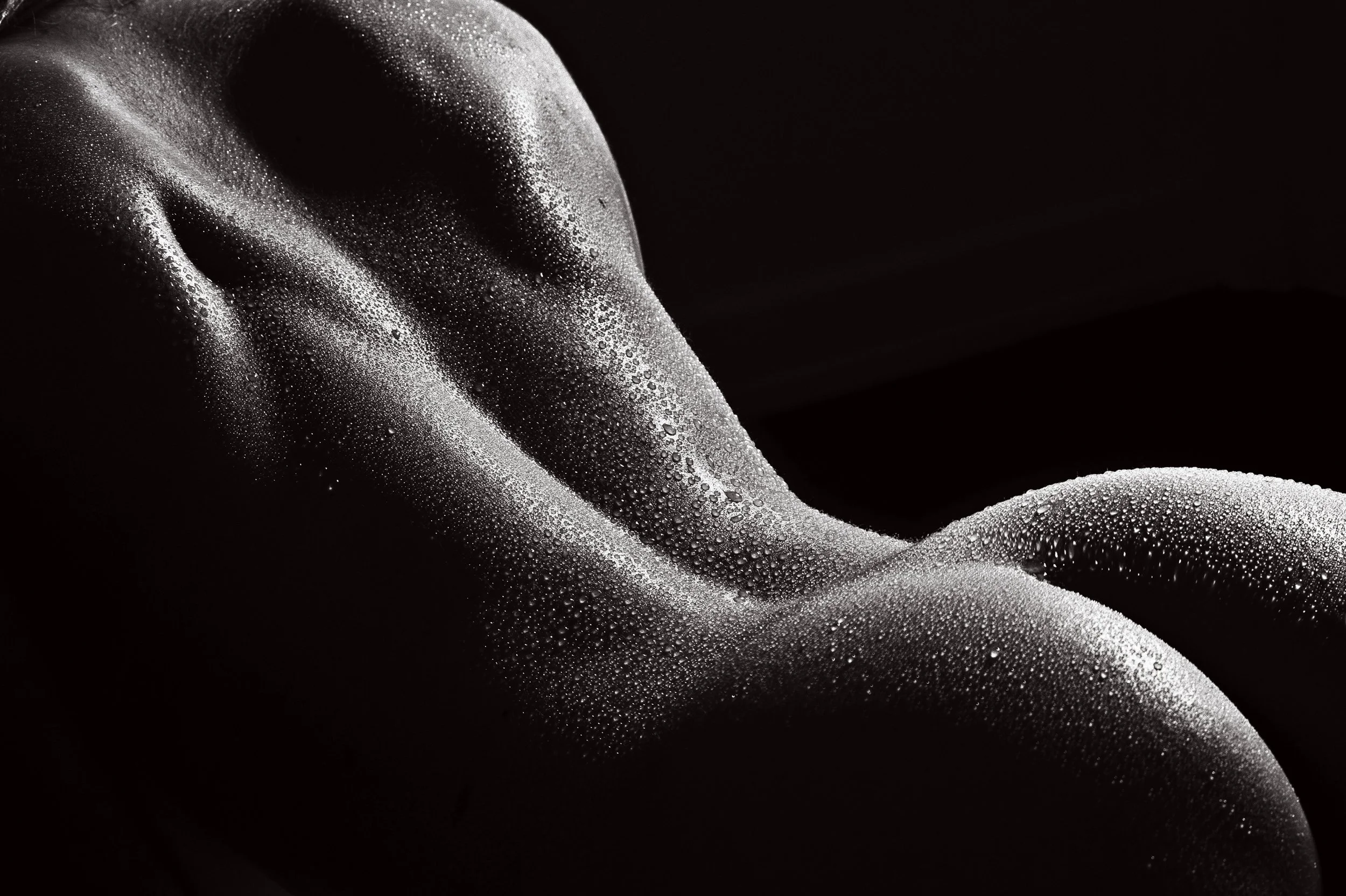 Une main en métal ou en plastique noir, recouverte de gouttelettes d'eau, repose sur une surface sombre. La lumière met en évidence la texture humide et lisse de la main et des gouttelettes.