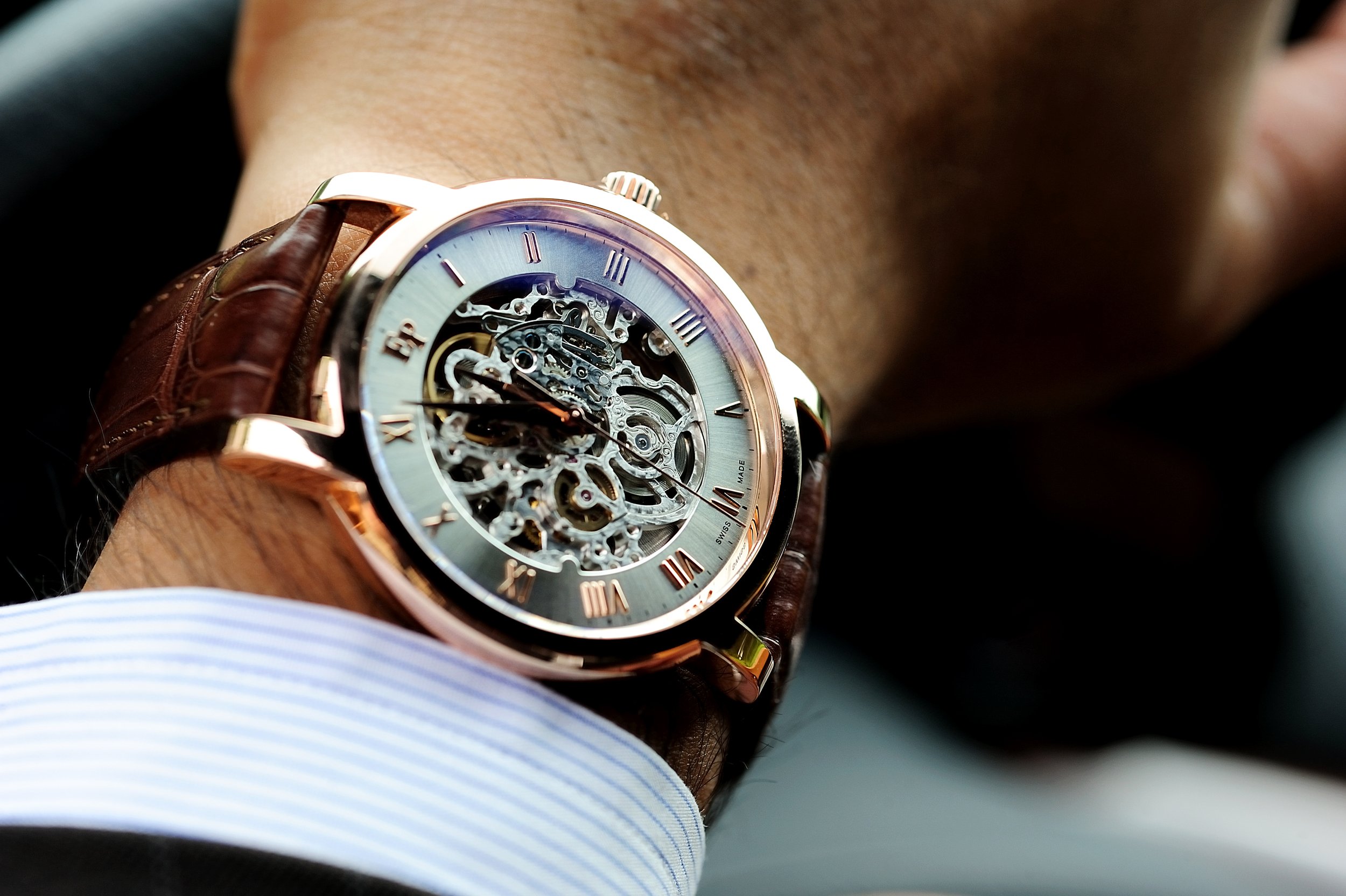 Montre-bracelet avec mécanisme squelette en or rose, portée au poignet d'une personne portant une chemise à rayures bleues et blanches.