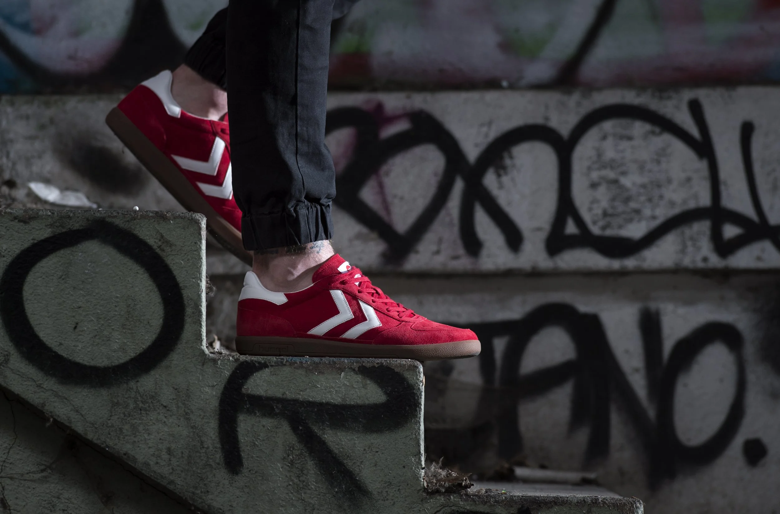 Chaussures de sport rouges et blanches portées par une personne debout sur un escalier en béton graffité dans un environnement urbain