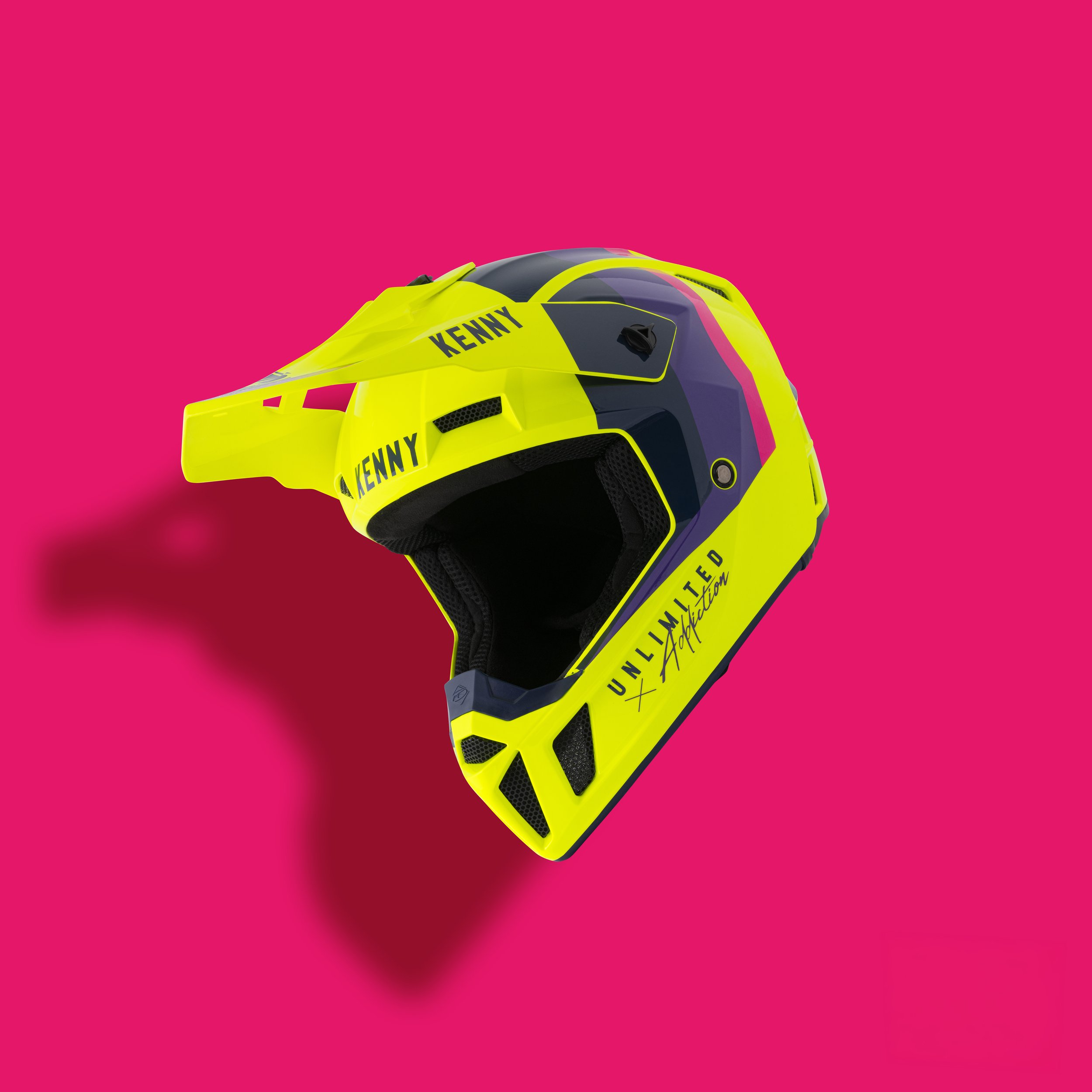 Casque de motocross jaune avec le nom 'KENNY' écrit dessus, placé sur un fond rose