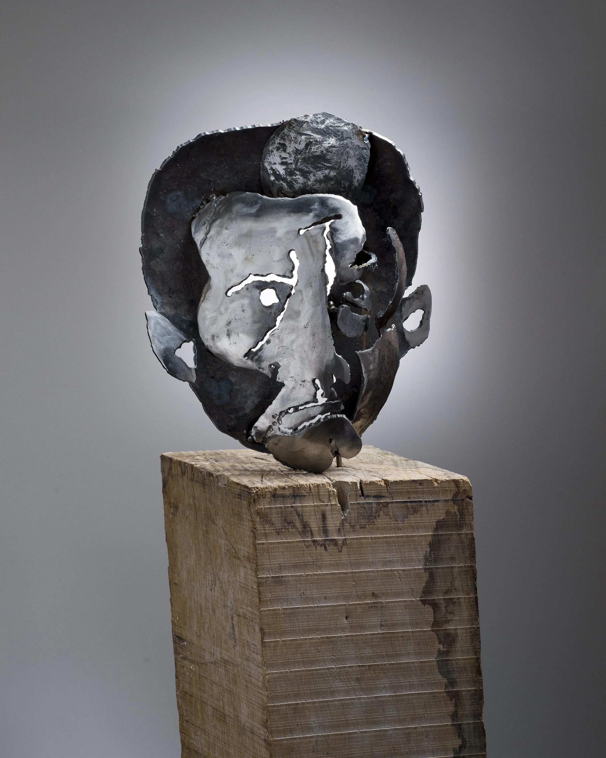 Sculpture abstraite en métal fixée sur un support en bois, présentant des formes ondulantes et creusées, avec une surface à la fois lisse et texturée, sur un fond gris neutre.