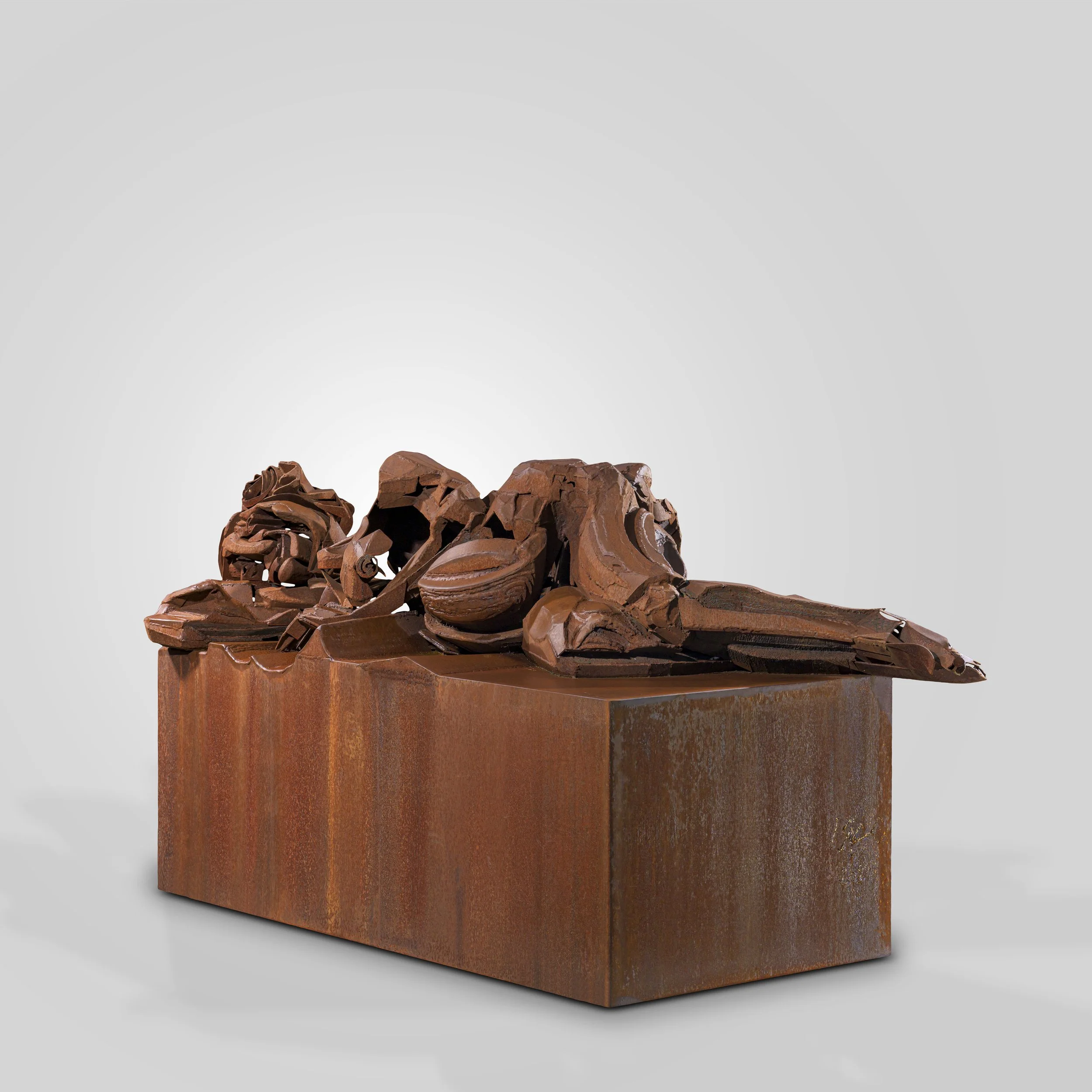 Une sculpture en acier corten représentant un lion couché, positionné sur un socle en métal, avec un fond gris clair.
