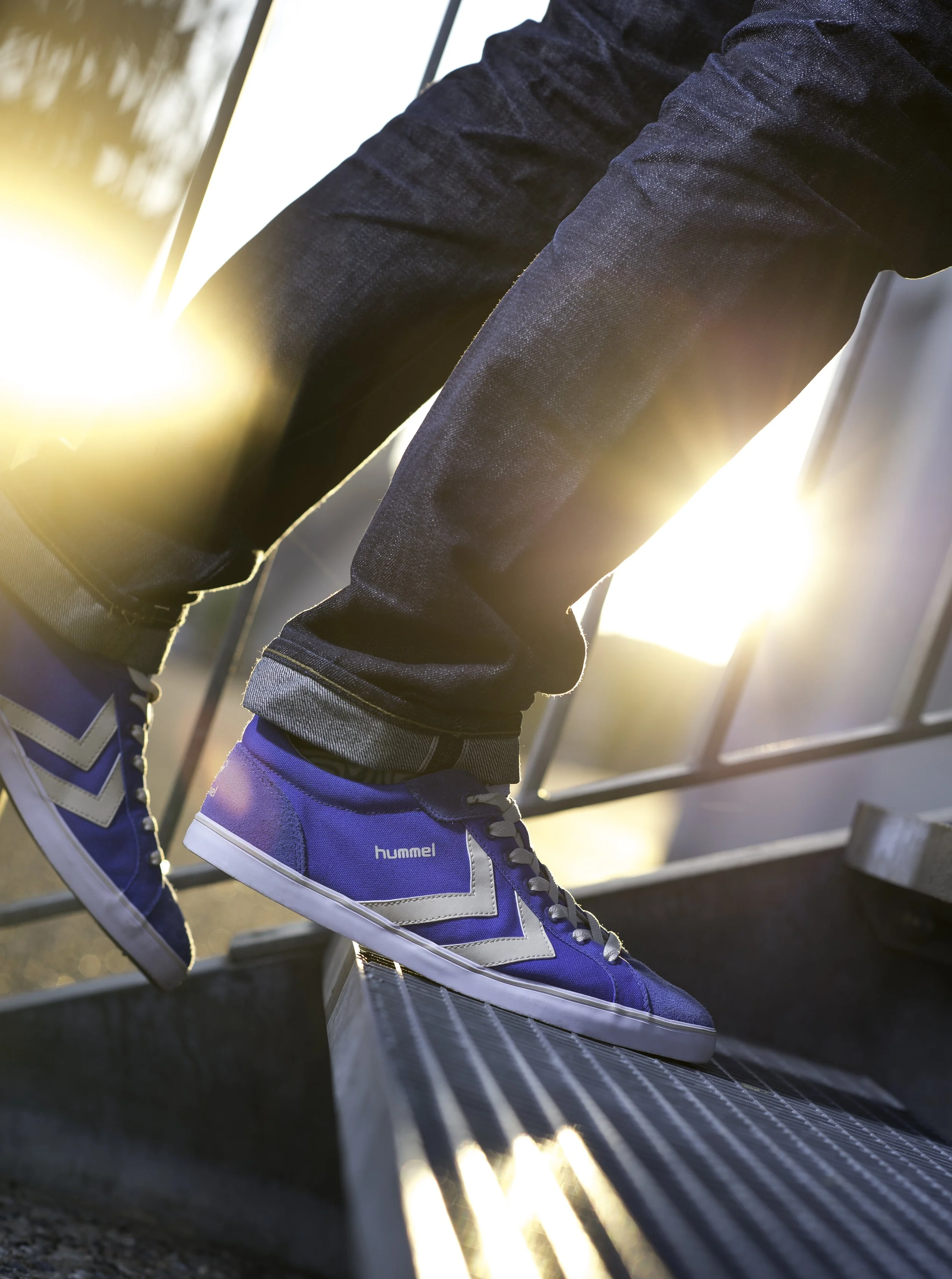 Baskets bleus de marque hummel, chaussures de sport enfilées, à côté d'une structure métallique, avec un fond de coucher de soleil.
