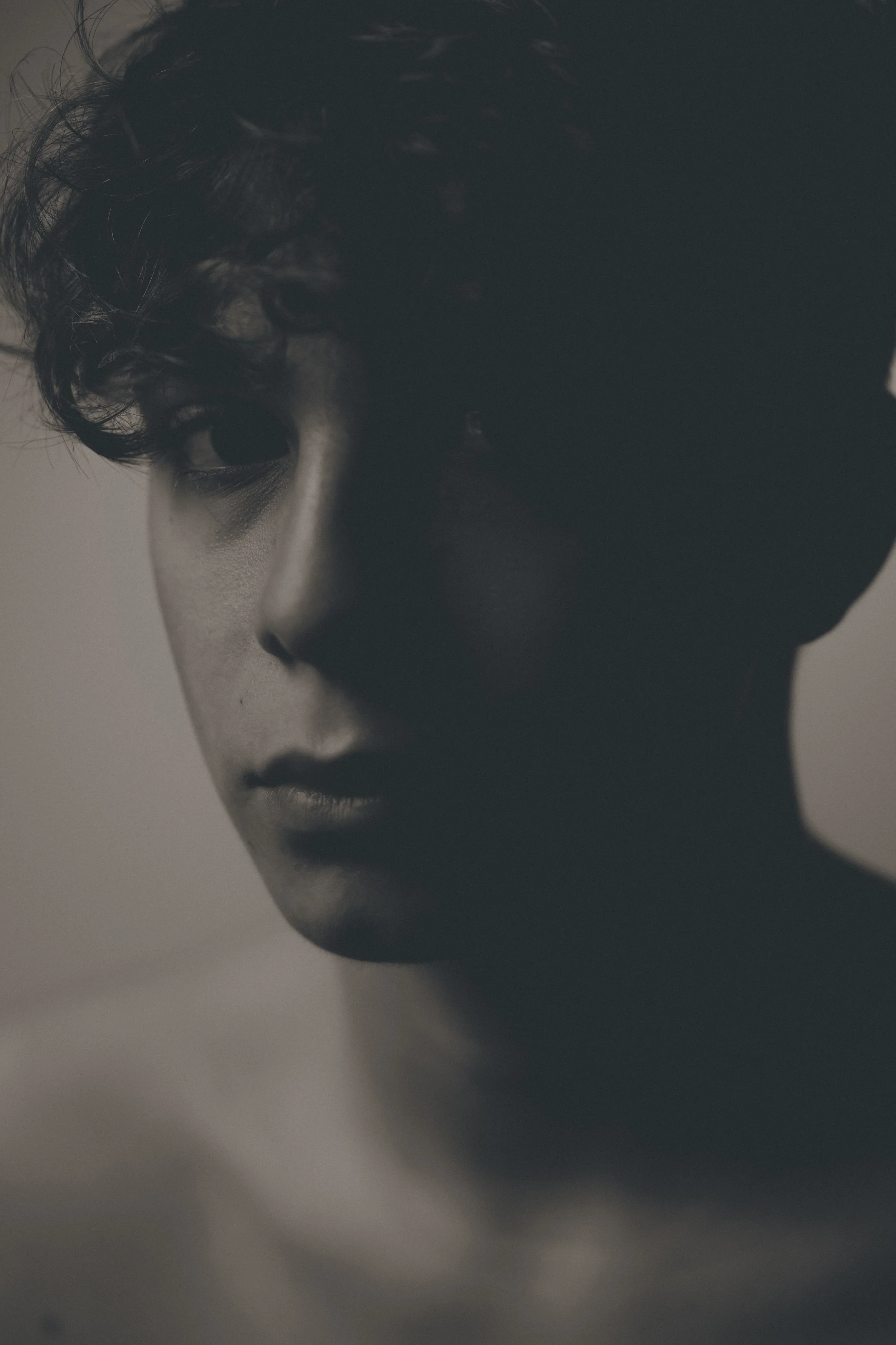 Portrait en noir et blanc d'un jeune homme avec cheveux bouclés, regardant vers le bas et de profil.