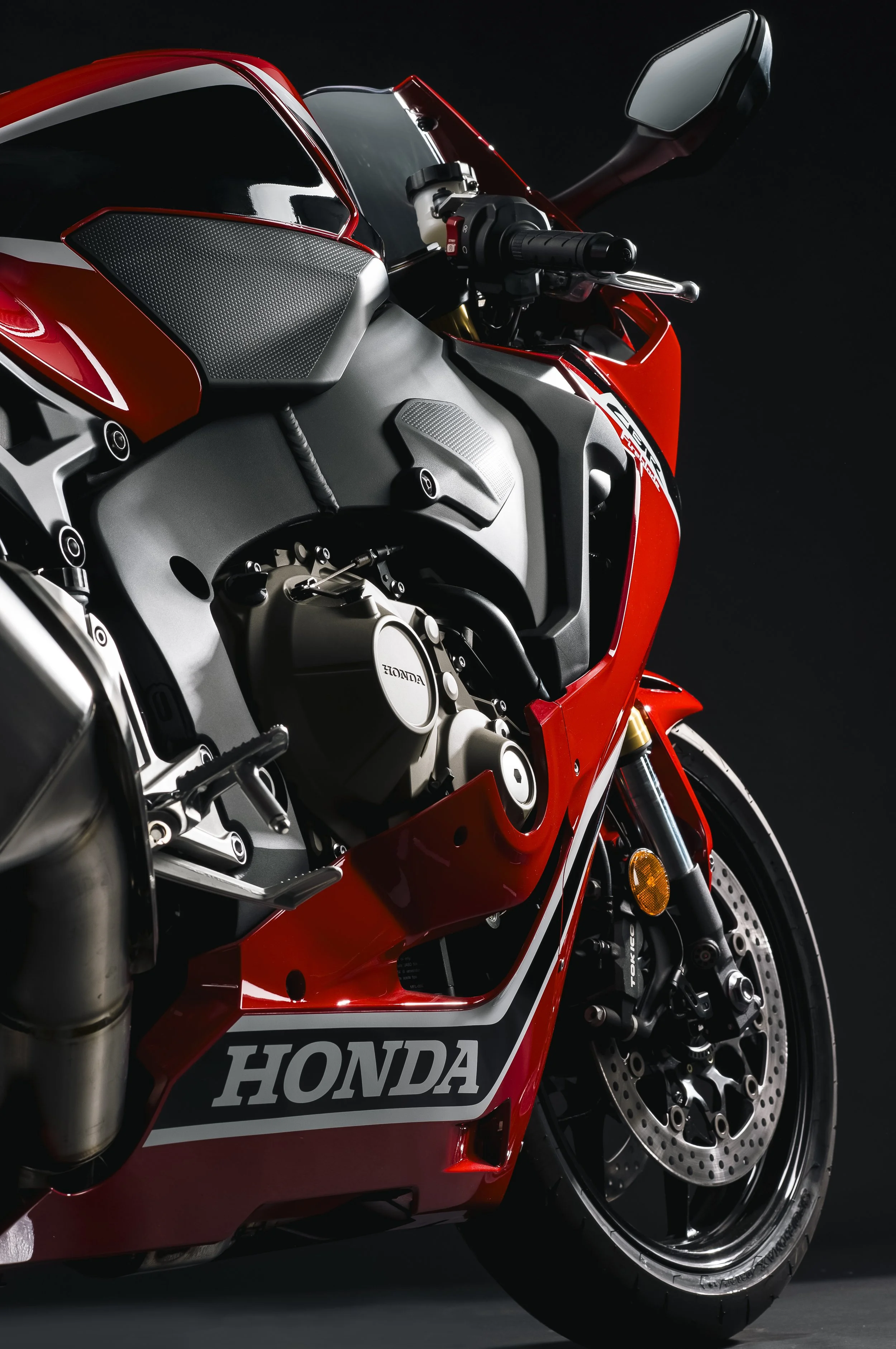 Une moto de course Honda rouge avec des détails noirs et blancs, affichée sur un fond noir.